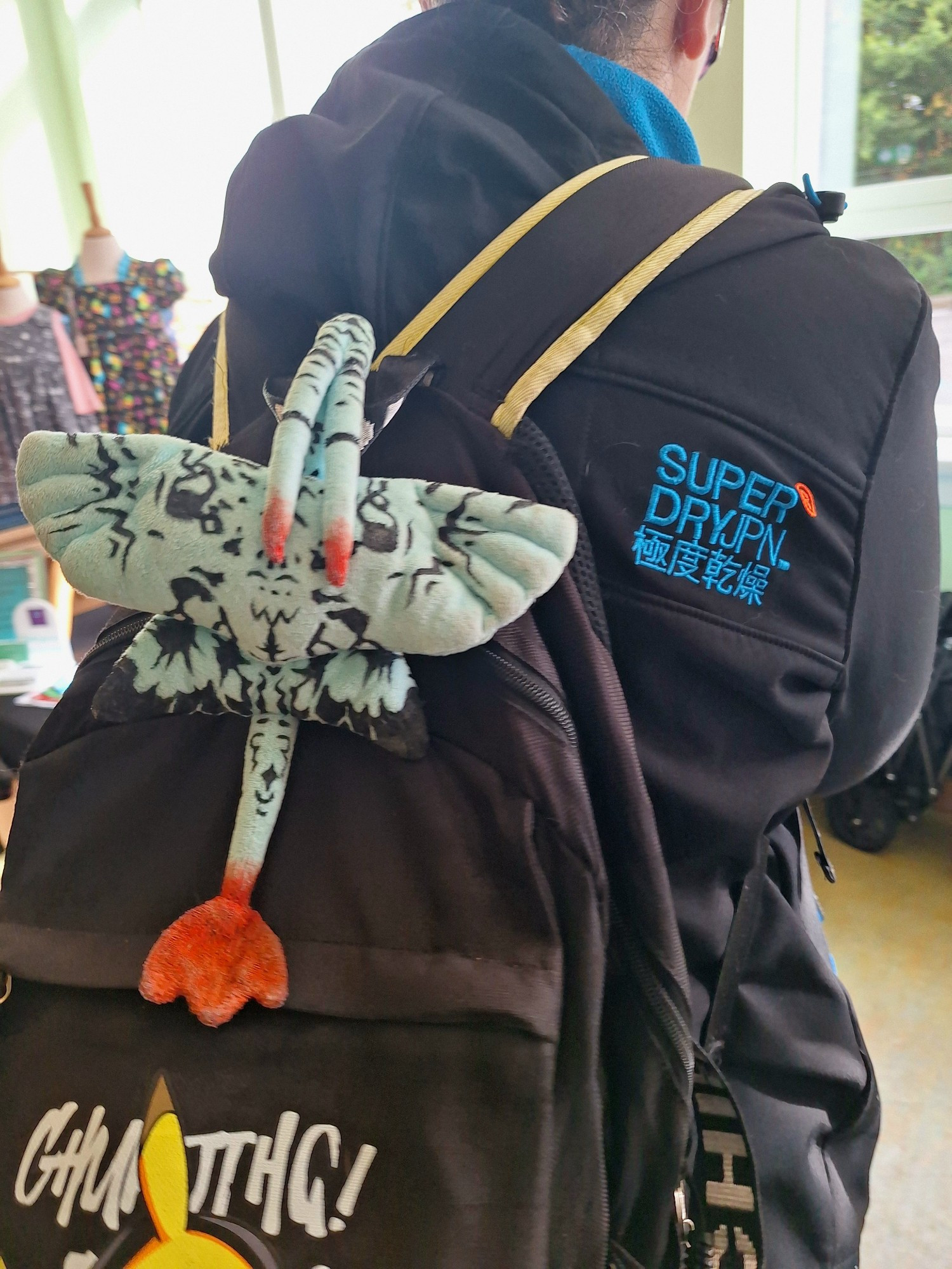 A woman standing in front of a rack of clothes. A banshee plush hangs from her bag without her knowledge.