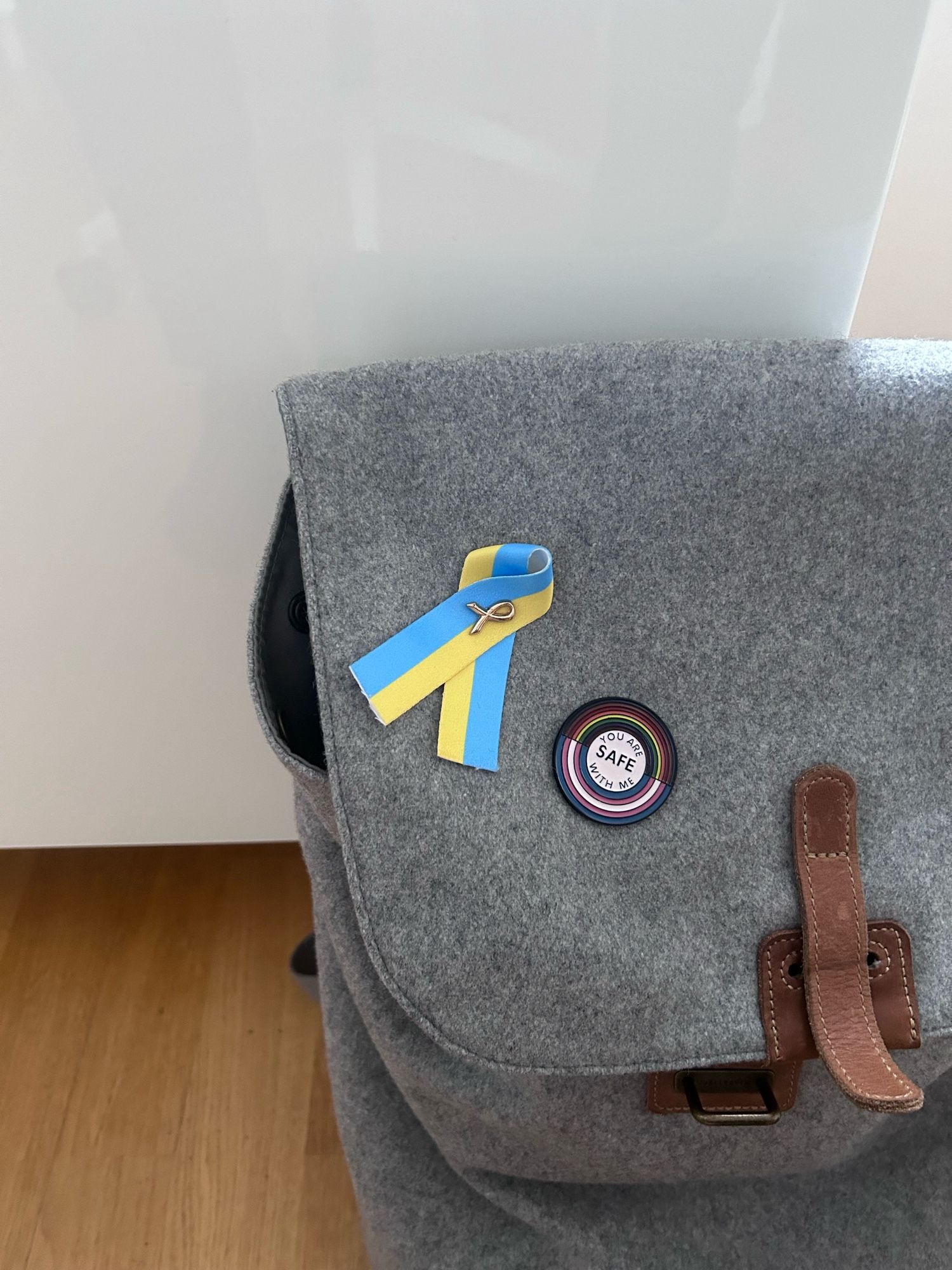 Grauer Rucksack mit einer blau-gelben Schleife als Pin und einem Regenbogen-Pin