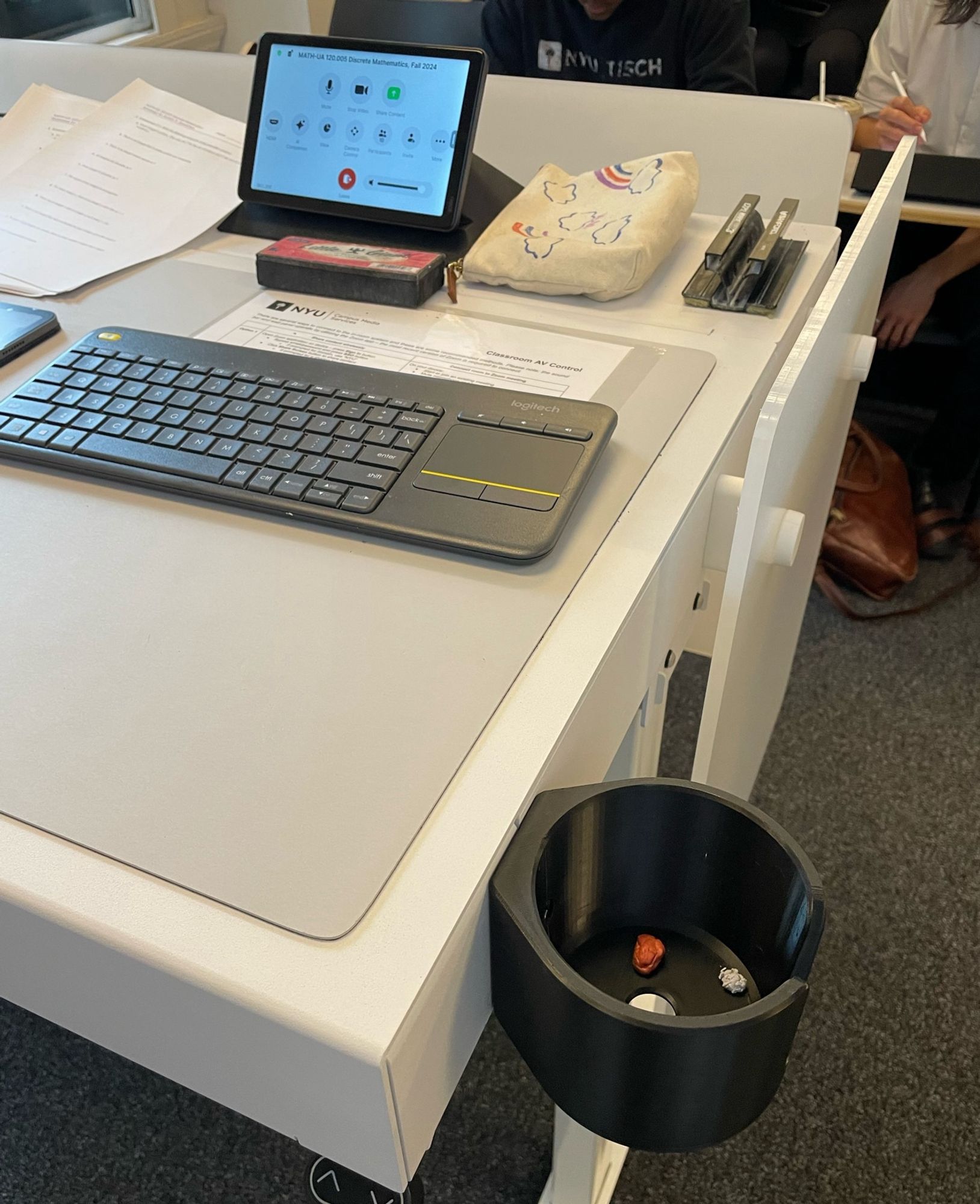 Beige standing desk with black outboard cup holder attached. Someone has left a wad of used chewing gum in the cup holder, along with a crumpled wrapper