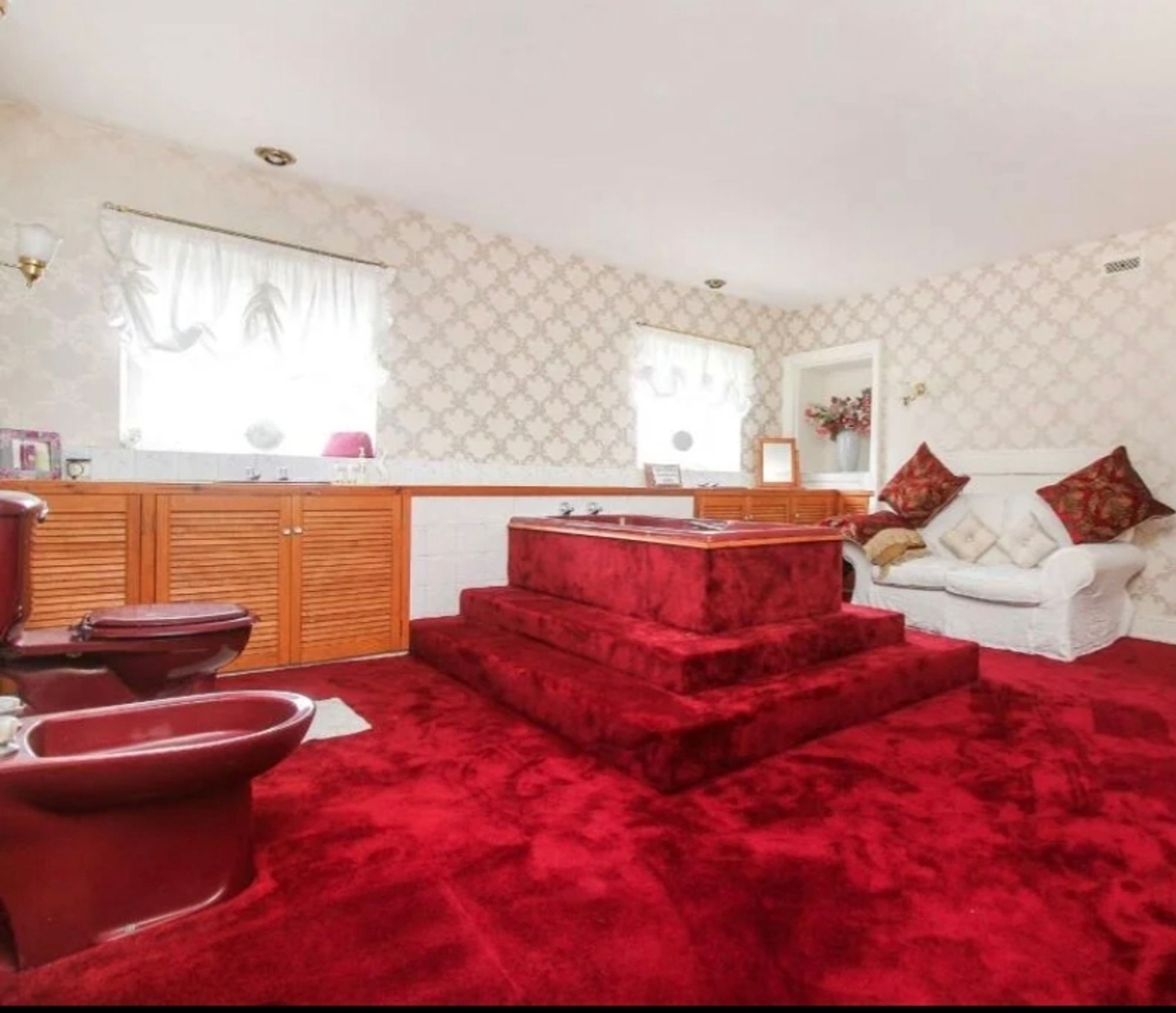 A fully carpeted bathroom with a red suite (incl bidet) with a sofa