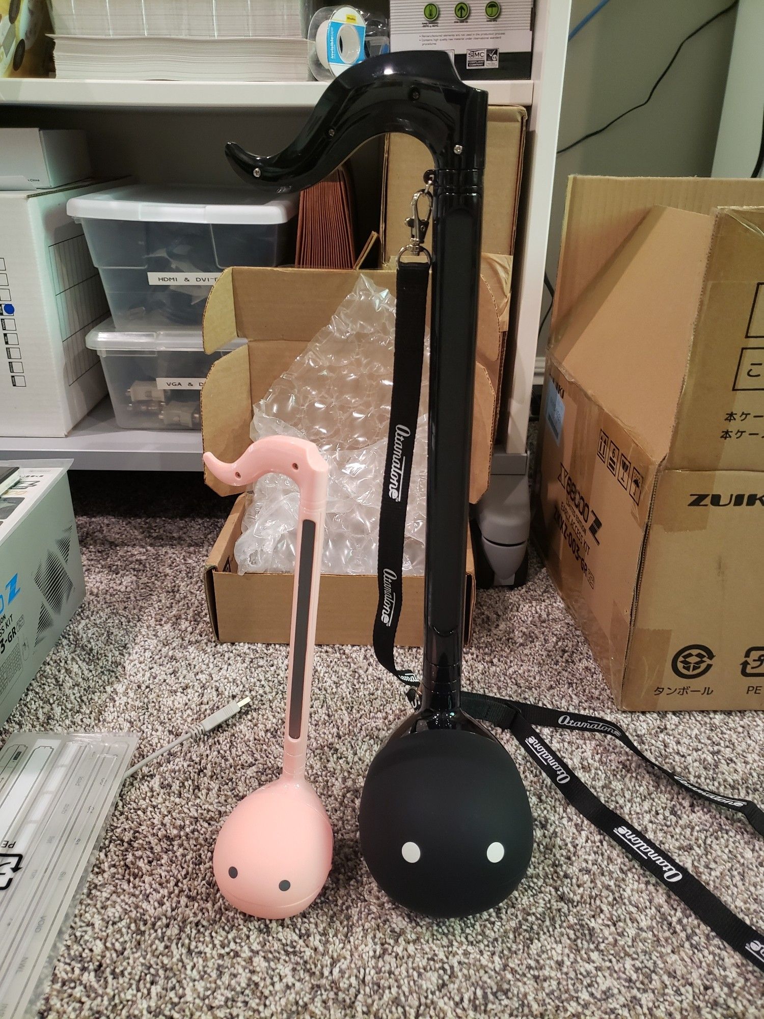 A regular pink Otamatone and a black Deluxe Otamatone