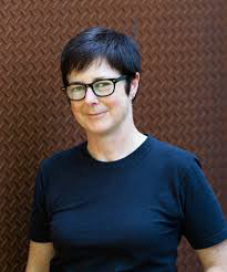 A woman with short dark cropped hair wearing dark rimmed glasses and a dark T-shirt