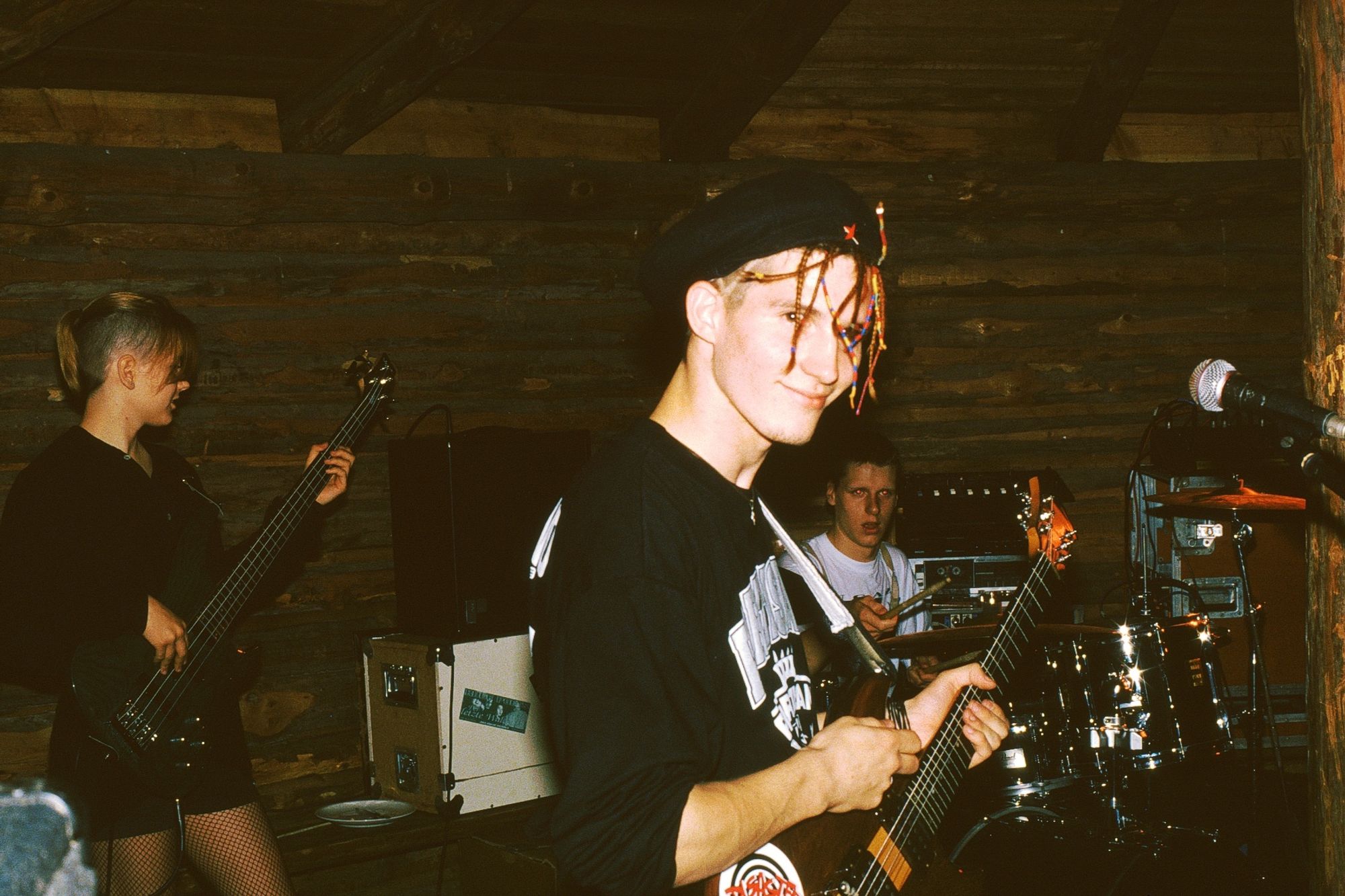 Ein Foto von einem Konzert mit Gitarre im Vordergrund, Basecap falschrum auf und darunter bunte dreads (oder sowas).
Im Hintergrund unsere Bassistin und der Drummer.