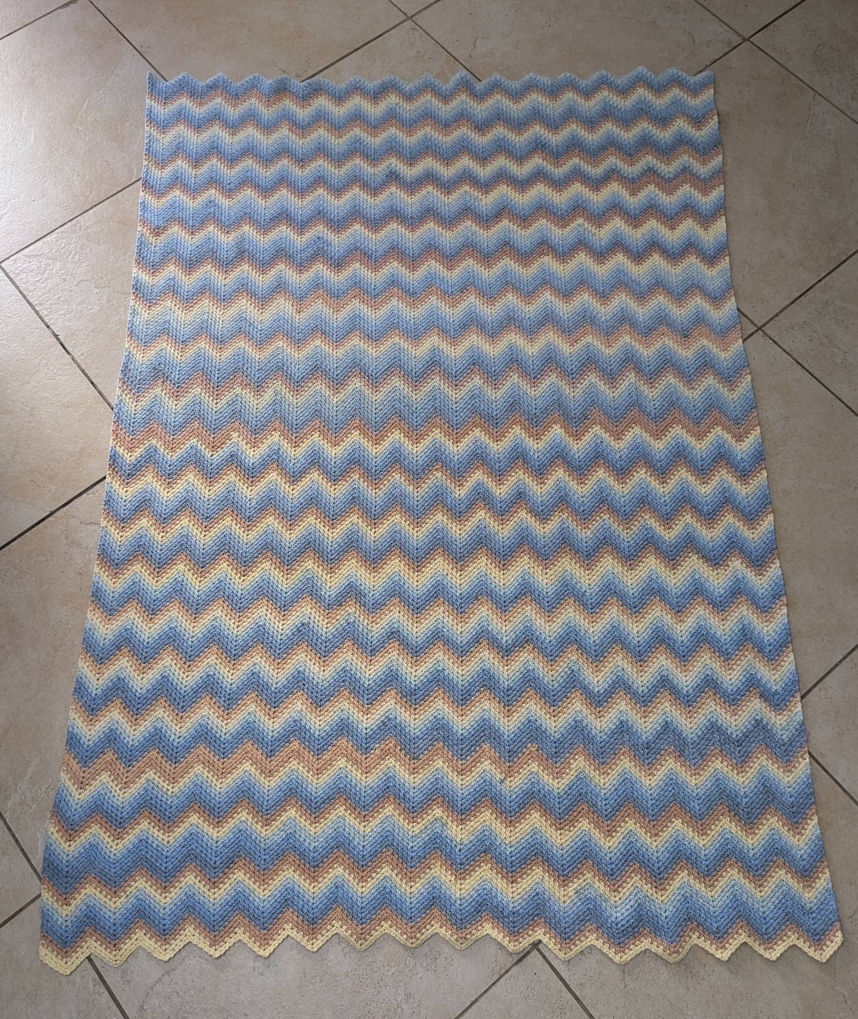 Zig zag moss stitch crochet blanket laid flat to show the size and color striping (yellow, orange, light to dark gray-blue)