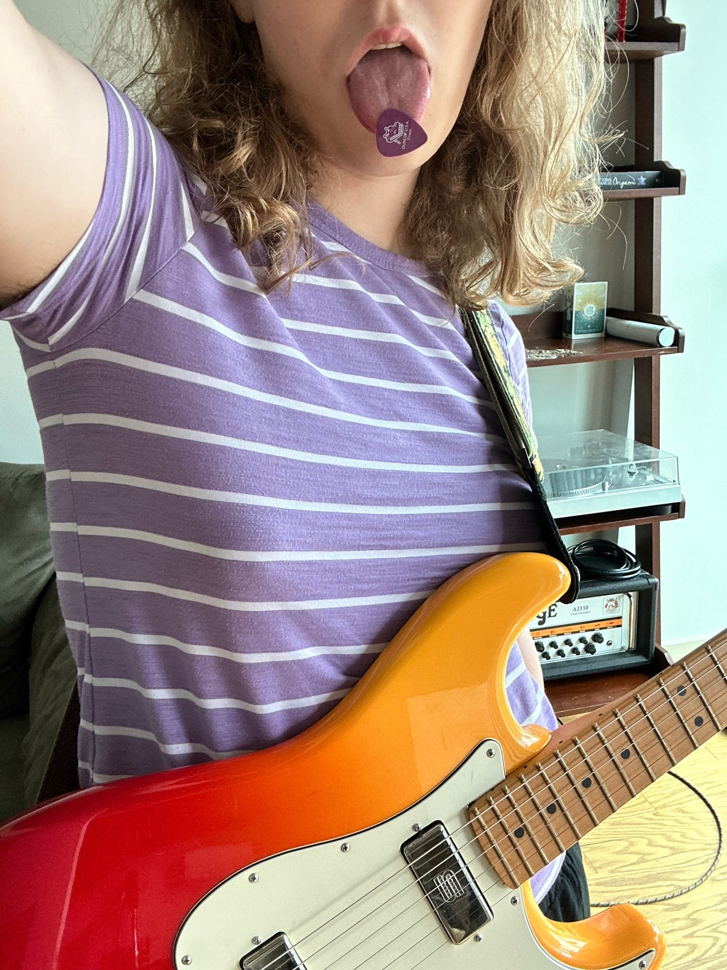 melody in a lilac colored shirt with white stripes and a guitar pick stuck to her tongue- she is playing on a tequila sunrise stratocaster