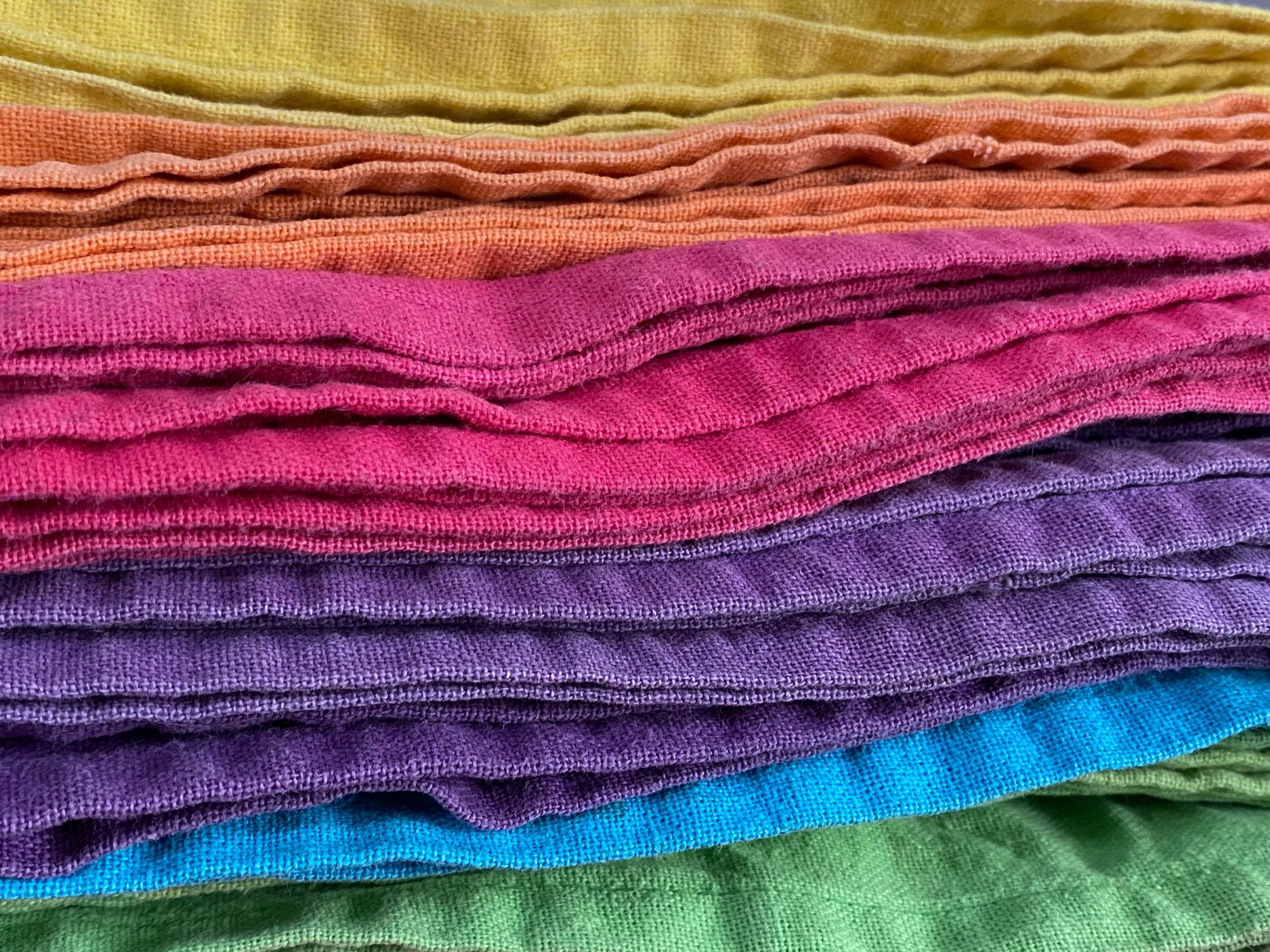 a stack rainbow coloured, tea-towels: yellow, orange, pink, purple, blue and green