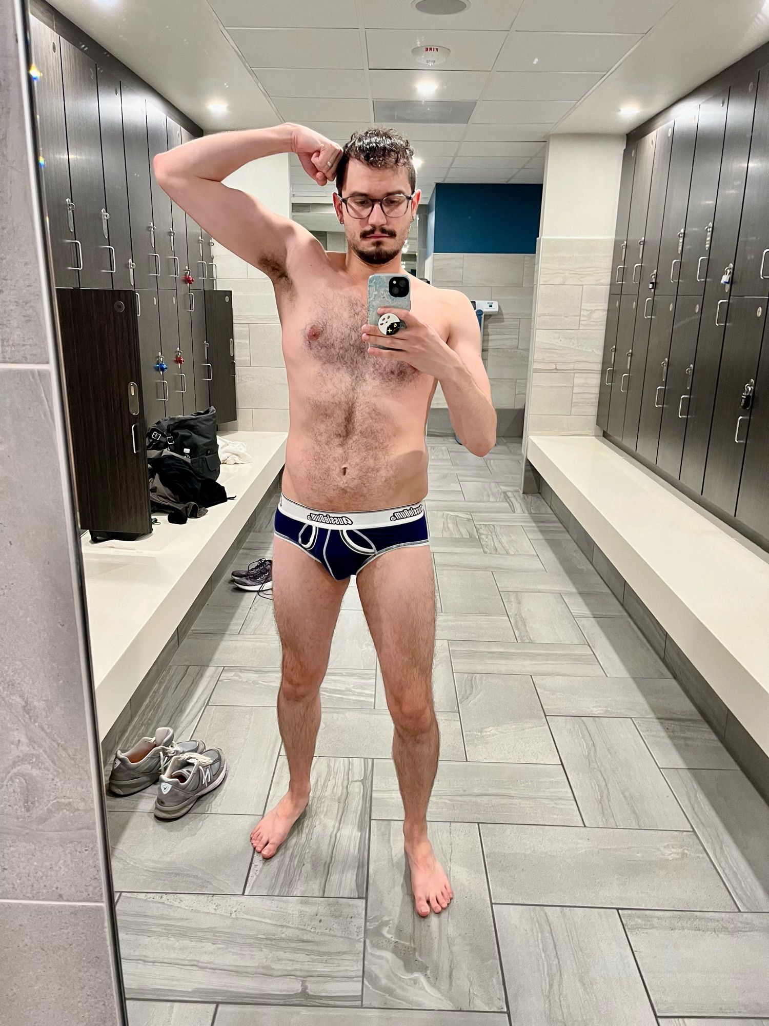 Rip sneaks a flex in the mirror despite the locker room being pretty busy. They’re wearing blue briefs because they’re still too nervous to wear a jock to the gym