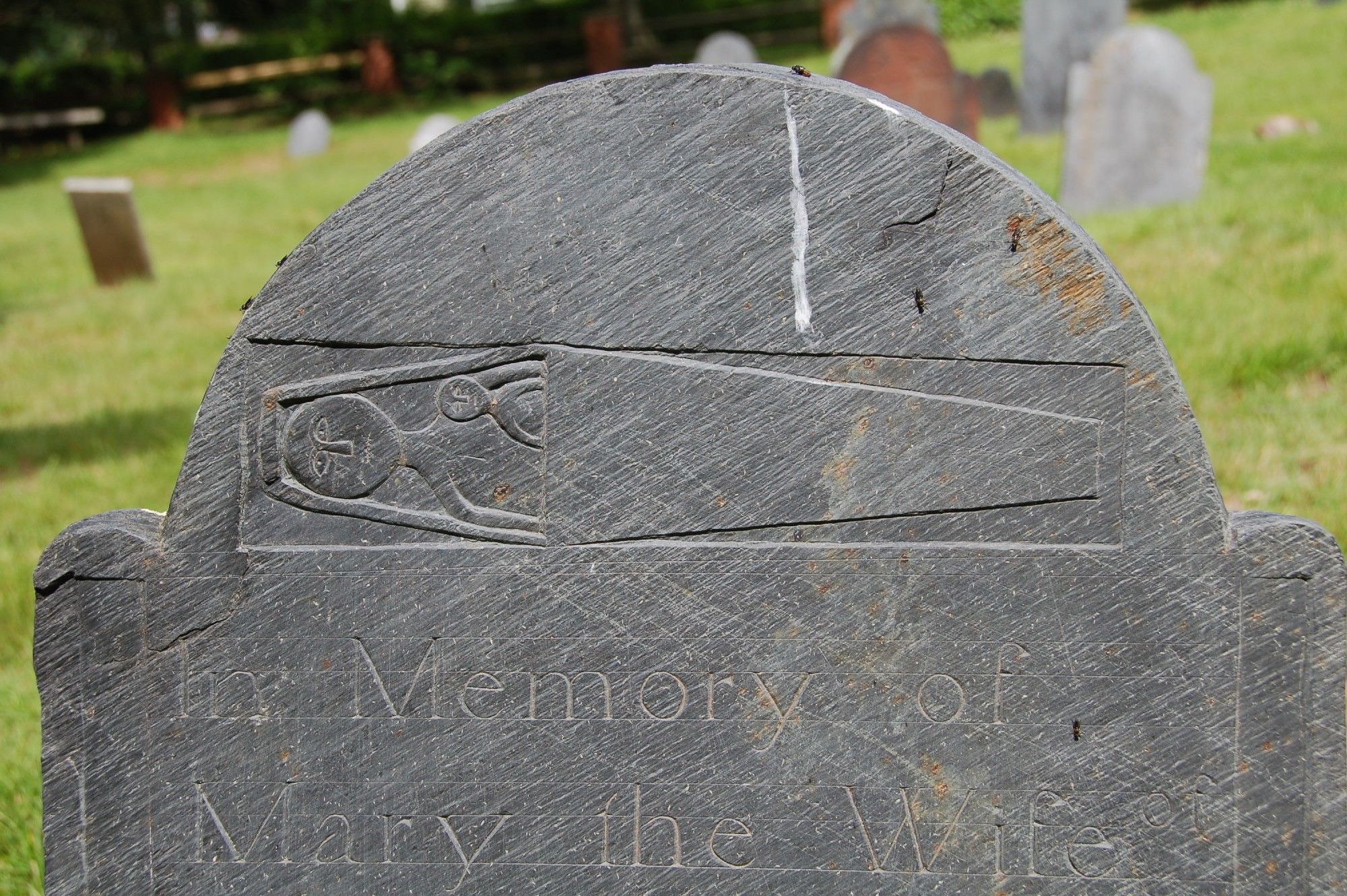 top of a gray slate gravestone
with an image of a horizontal coffin
containing a large figure and a tiny figure