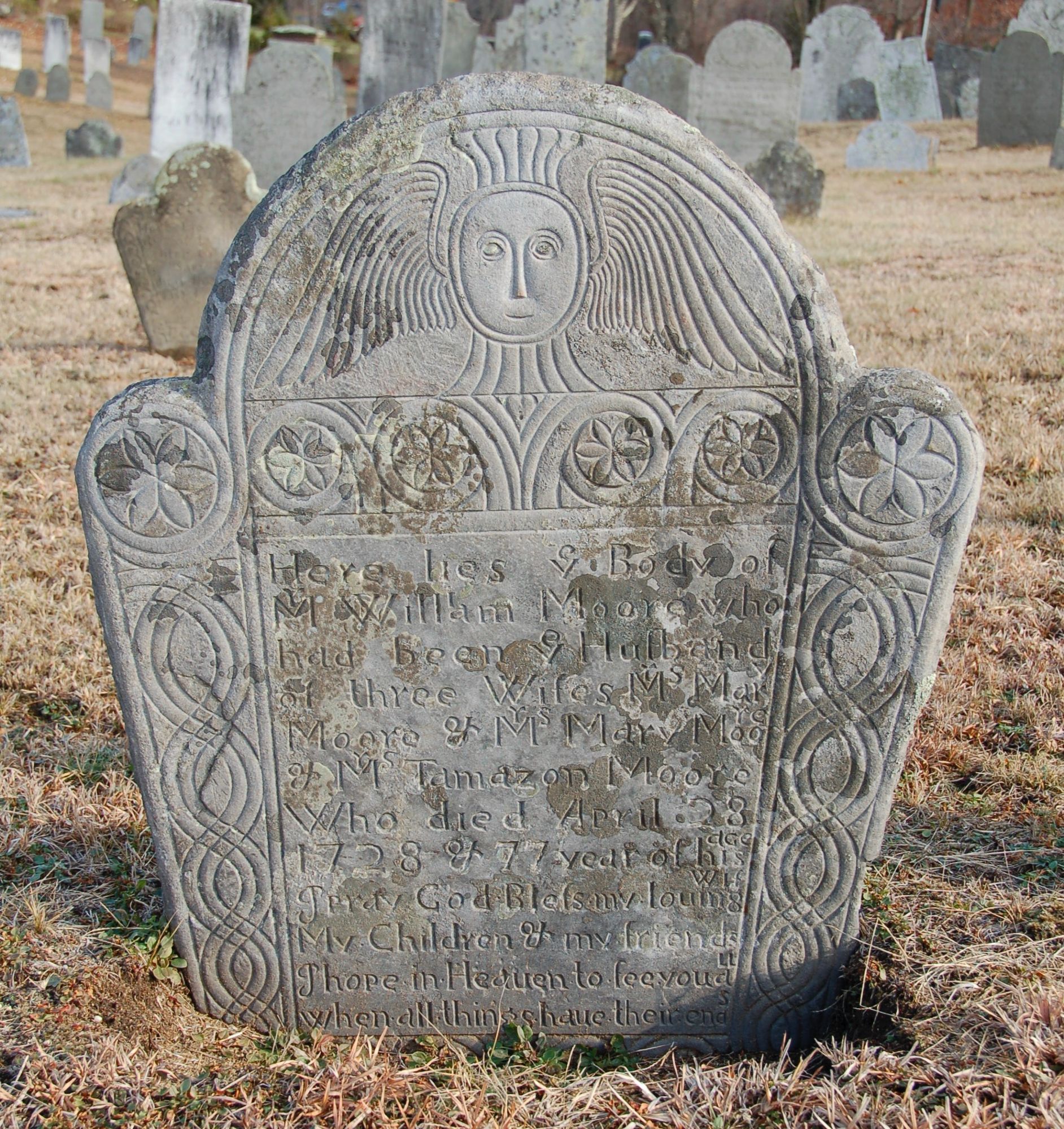 gray gravestone with rosettes, winged soul effigy, and lichen on surface

epitaph:

Here lies ye Body of 
Mr William Moore who 
had been ye Husband 
of three Wifes Mrs Mary 
Moore & Mrs Mary Moore 
& Mrs Tamazon Moore 
Who died April 28 
1728 & 77 year of his age 
I pray God Bless my louing Wif 
My Children & my friends
I hope in Heauen to see you all
when all things have their ends