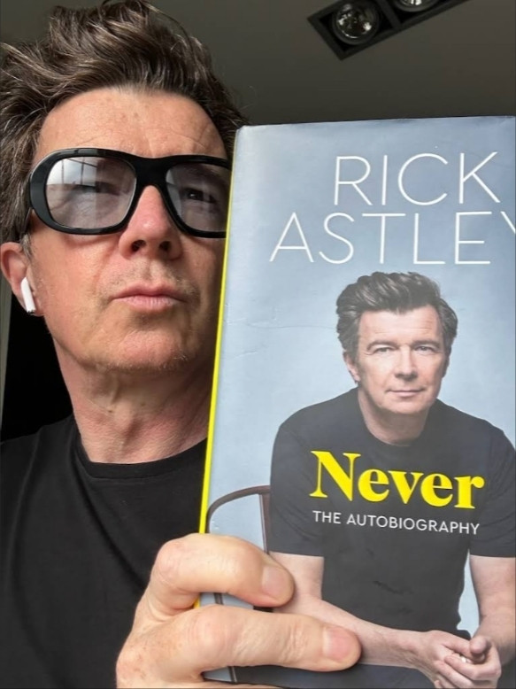 Rick Astley holding a copy of his new autobiography, titled 'Never'