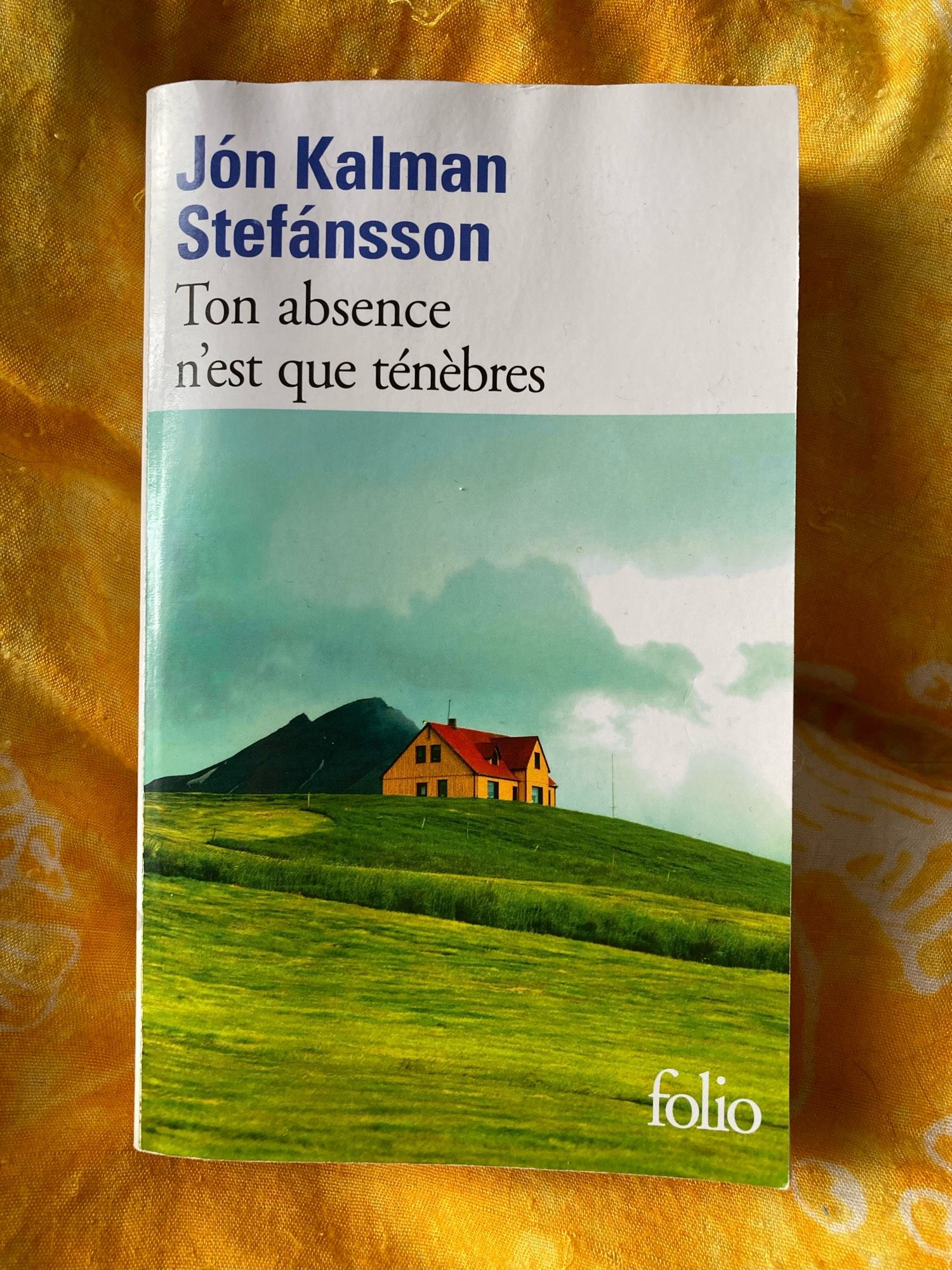 Couverture de l’édition folio du livre Ton absence n’est que ténèbres de Jón Kalman Stefánsson. On y voit une maison orange à toit rouge au milieu d’un paysage verdoyant.