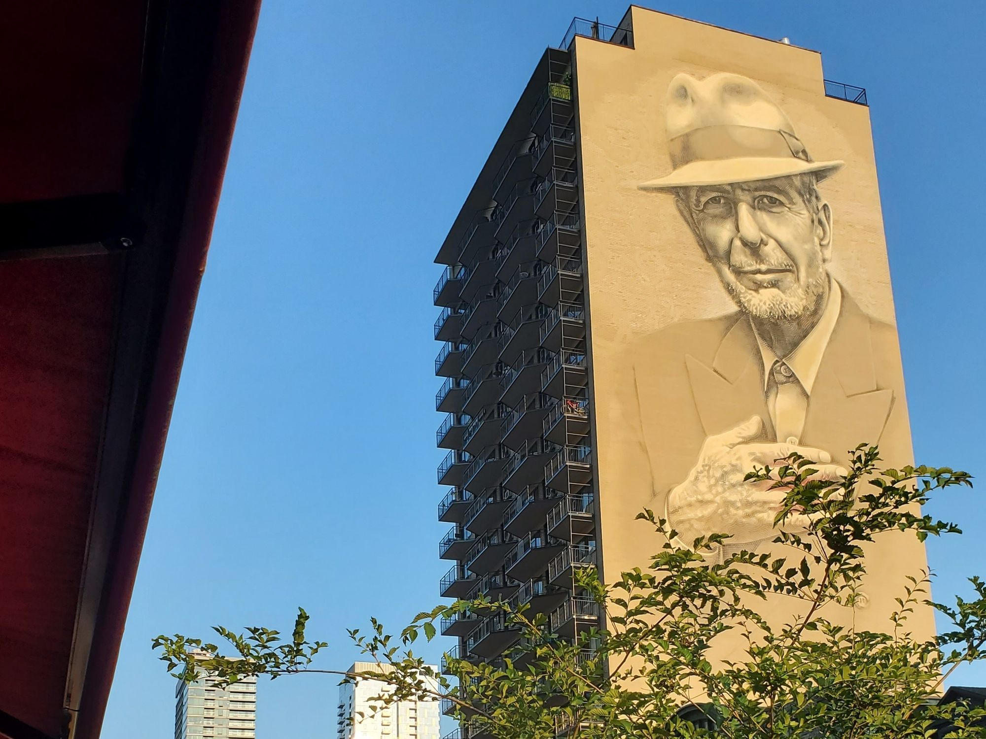 A mural of Leonard Cohen against a blue sky.