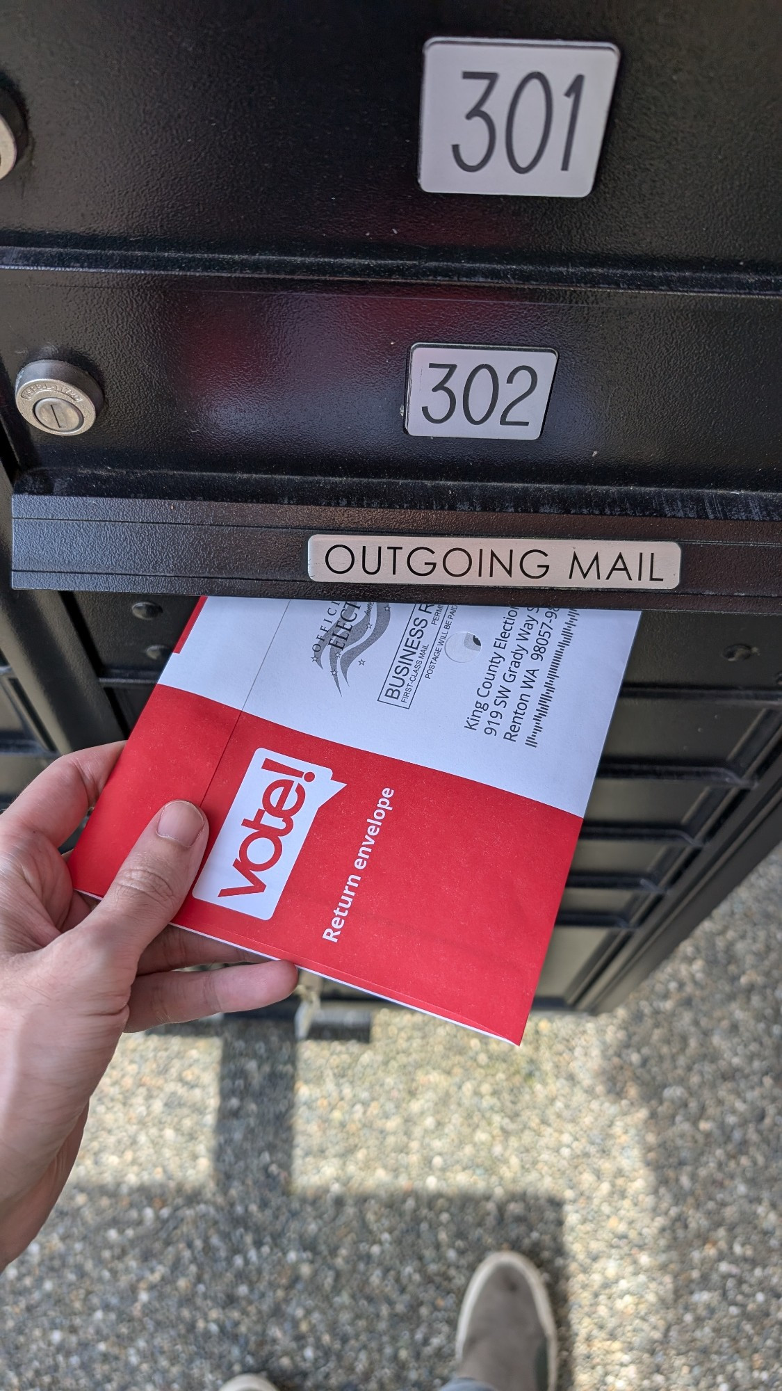 A voter envelope being placed into Outgoing Mail slot in mailbox