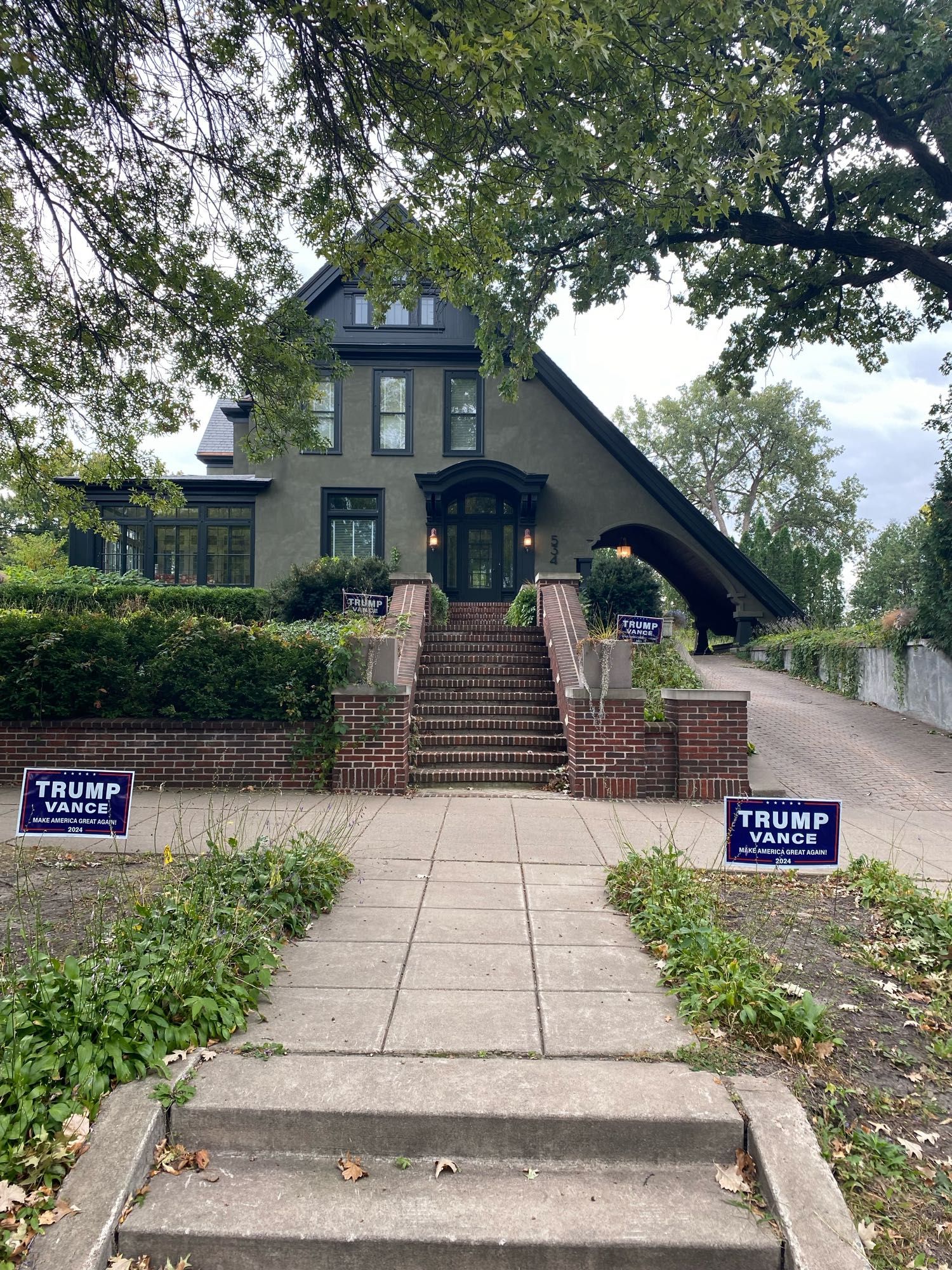 Multi-million house on Summit Ave with sloping carriageway roof over driveway, two Drumpf campaign signs in front yard and two placed illegally in the public ROW in boulevard.