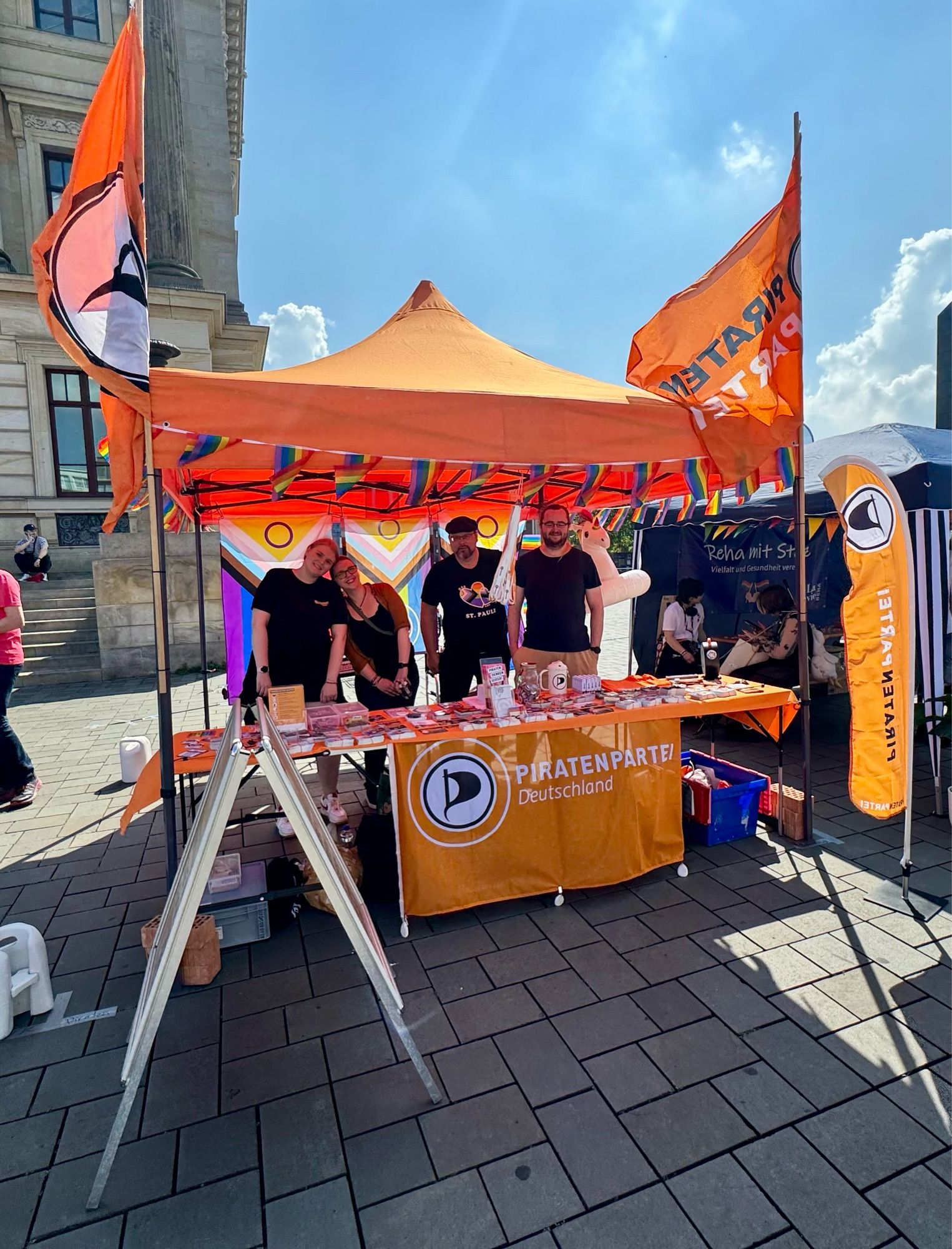 Ein Informationsstand der Piraten Braunschweig auf dem Schlossplatz und Braunschweig. Es sind Fahnen Aufkleber und mehrere Menschen zu sehen