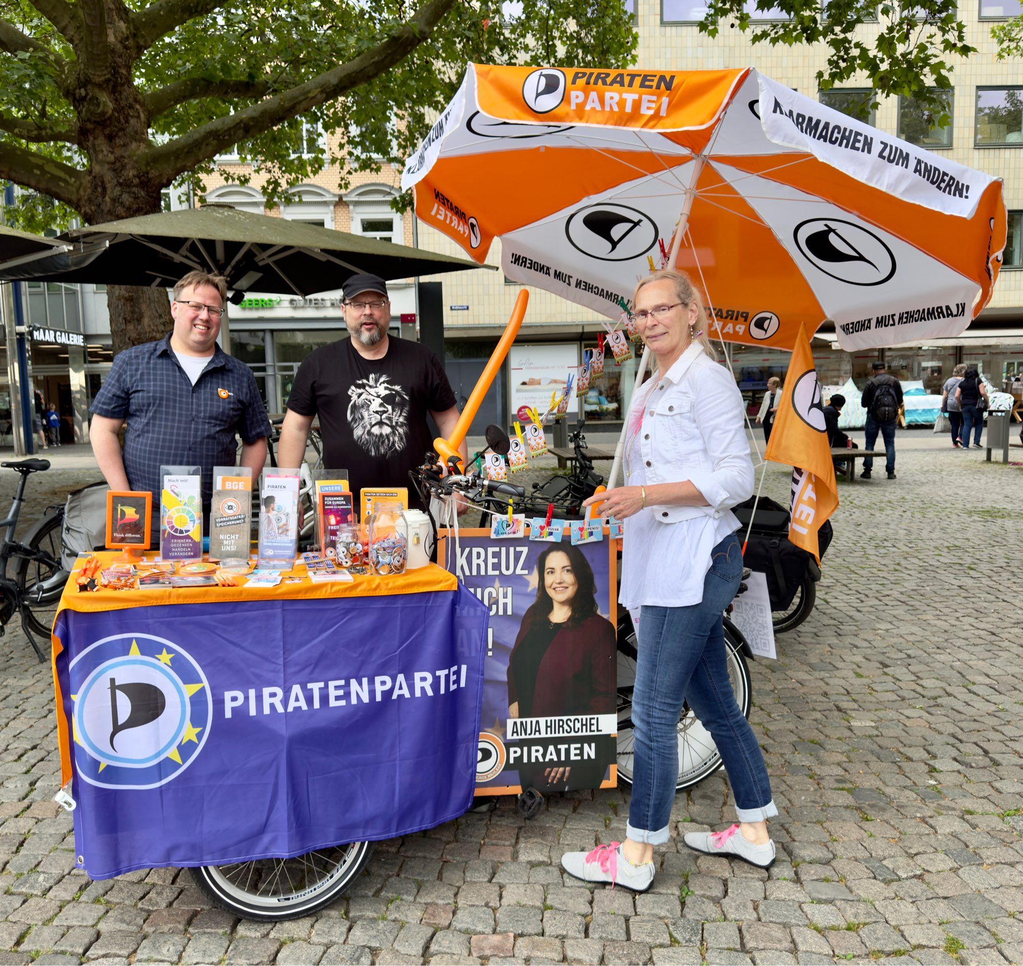 Ein Infostand der Piraten Partei aufgebaut auf einem lastenrad mit 3 Personen