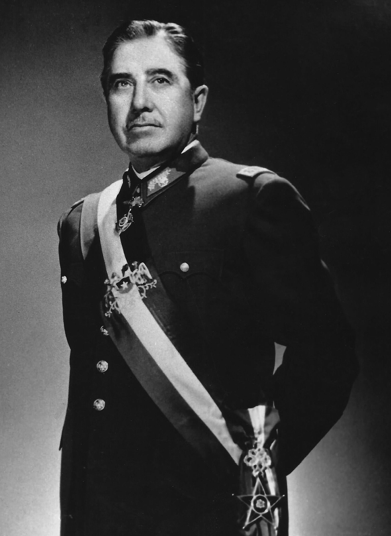 Official portrait, c. 1974, in a dark uniform with a sash in Chilean colours