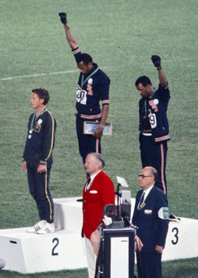 Gold medalist Tommie Smith and bronze medalist John Carlos showing the raised fist on the podium after the 200 m race at the 1968 Summer Olympics; both wear Olympic Project for Human Rights badges. Peter Norman from Australia also wears an OPHR badge in solidarity with Smith and Carlos.