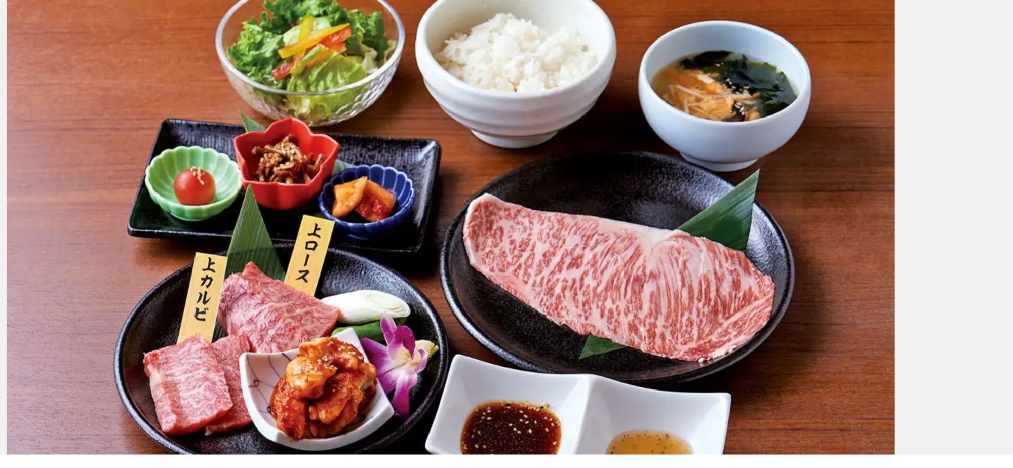 (Yakiniku Set): A beautifully arranged yakiniku meal featuring premium cuts of beef, side dishes, salad, rice, and miso soup.