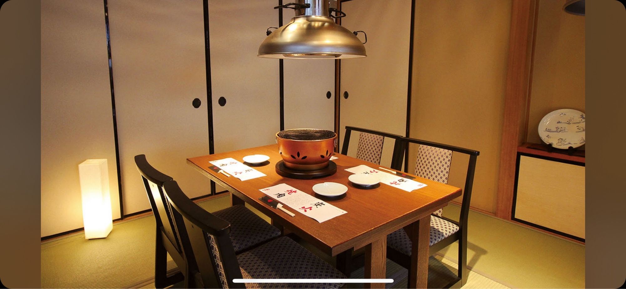 (Dining Room): A cozy traditional Japanese dining room with a wooden table and a grill set in the center, ready for yakiniku.