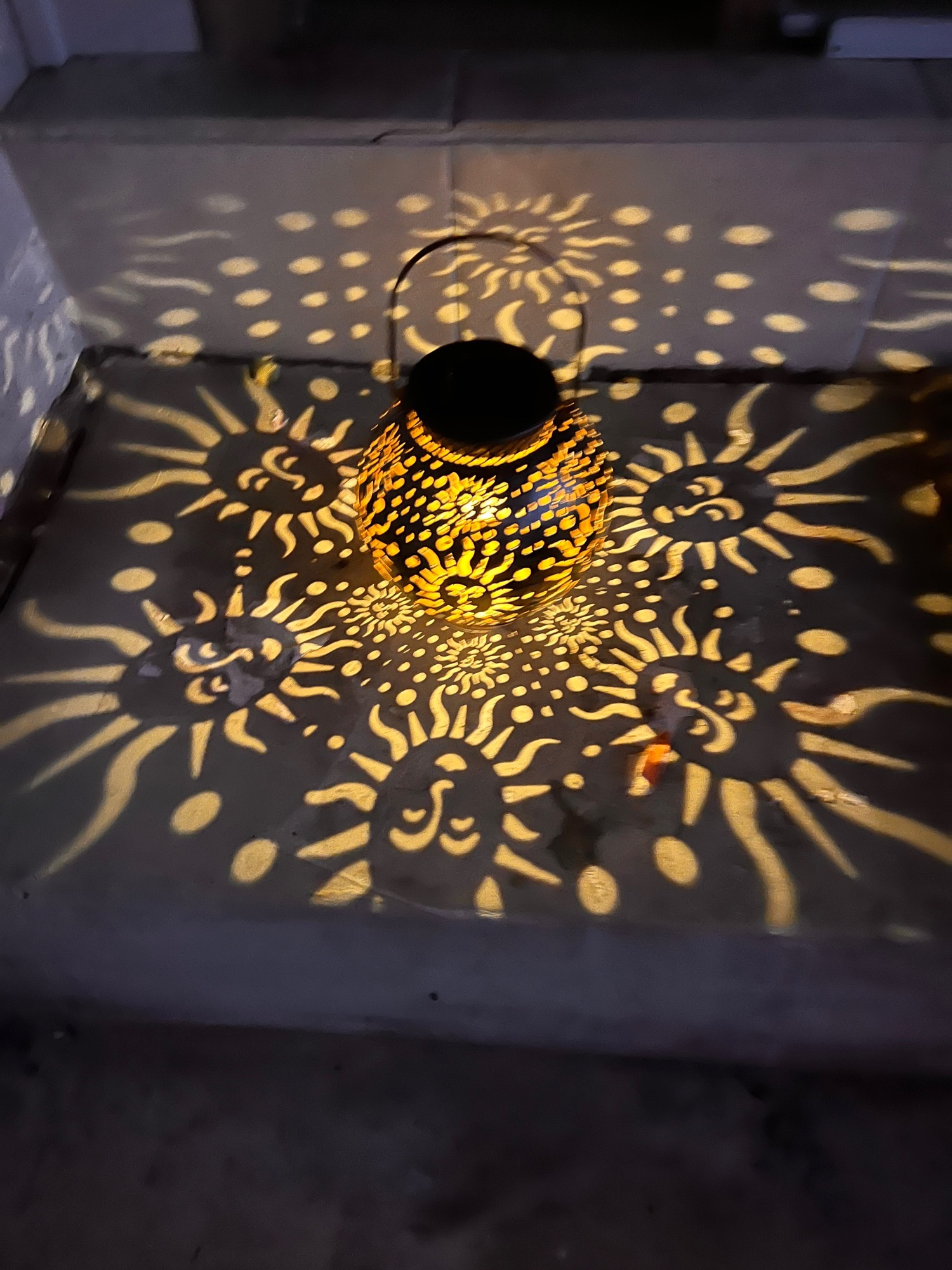 Lantern with sun pattern illuminating cutouts.