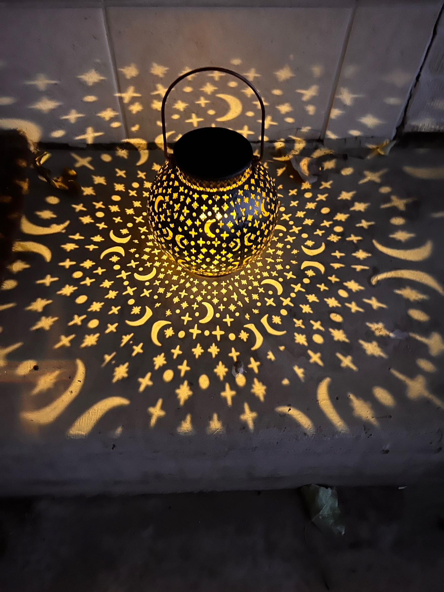 Lantern with moon pattern illuminating cutouts.