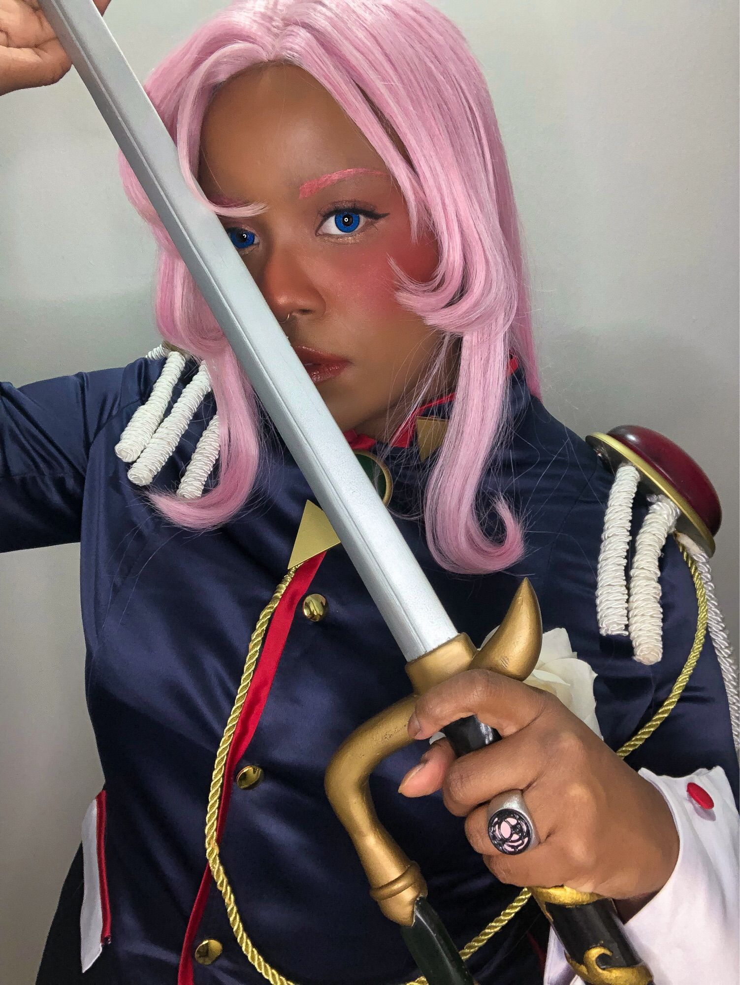 Na foto, a cosplayer kamijupiter vestida como a personagem Utena Tenjou, de Revolutionary Girl Utena. Ela está com uma peruca rosa, um blazer azul escuro com acessórios, espada e um anel de rosa na mão.