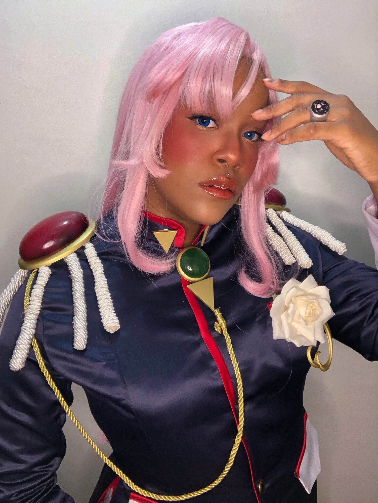 Na foto, a cosplayer kamijupiter vestida como a personagem Utena Tenjou, de Revolutionary Girl Utena. Ela está com uma peruca rosa, um blazer azul escuro com acessórios e um broche de rosa branca no peito.