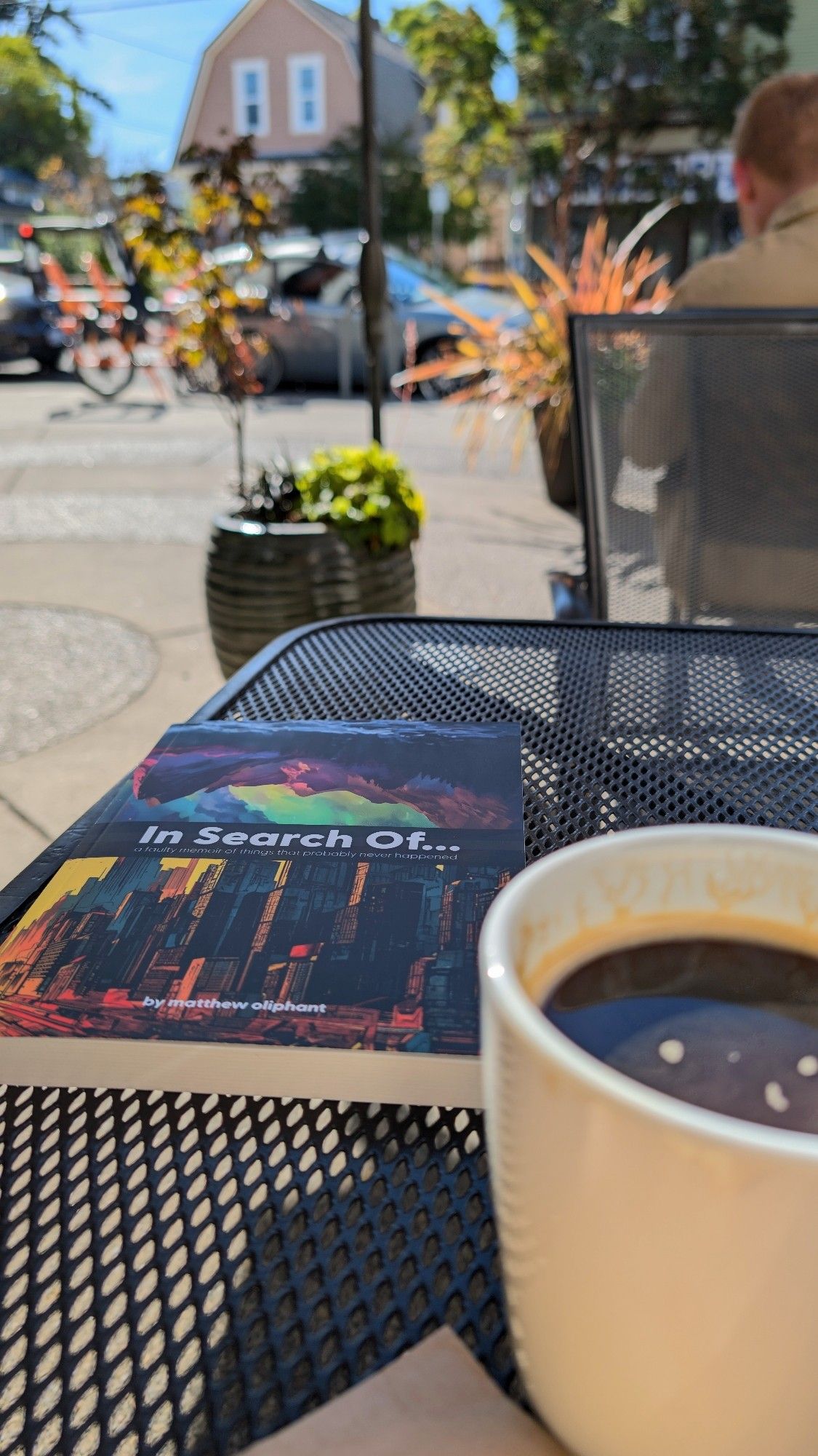 Picture of my novel on the outside table at the cafe. Coffee cup in foreground.