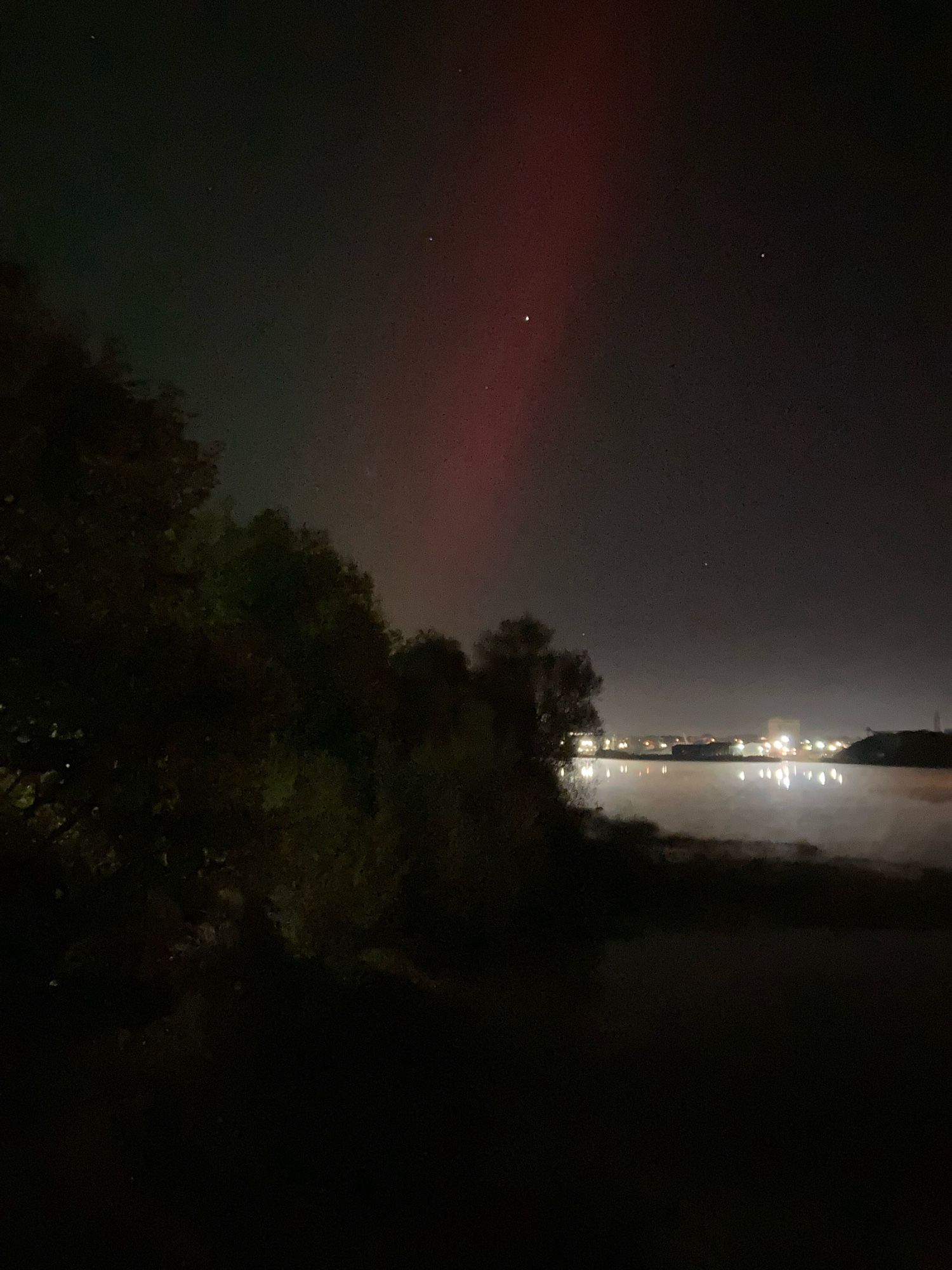 A view of Limerick from the east, looking over a very still Shannon. There’s a red streak in the sky. You can see the outline of a few swans.