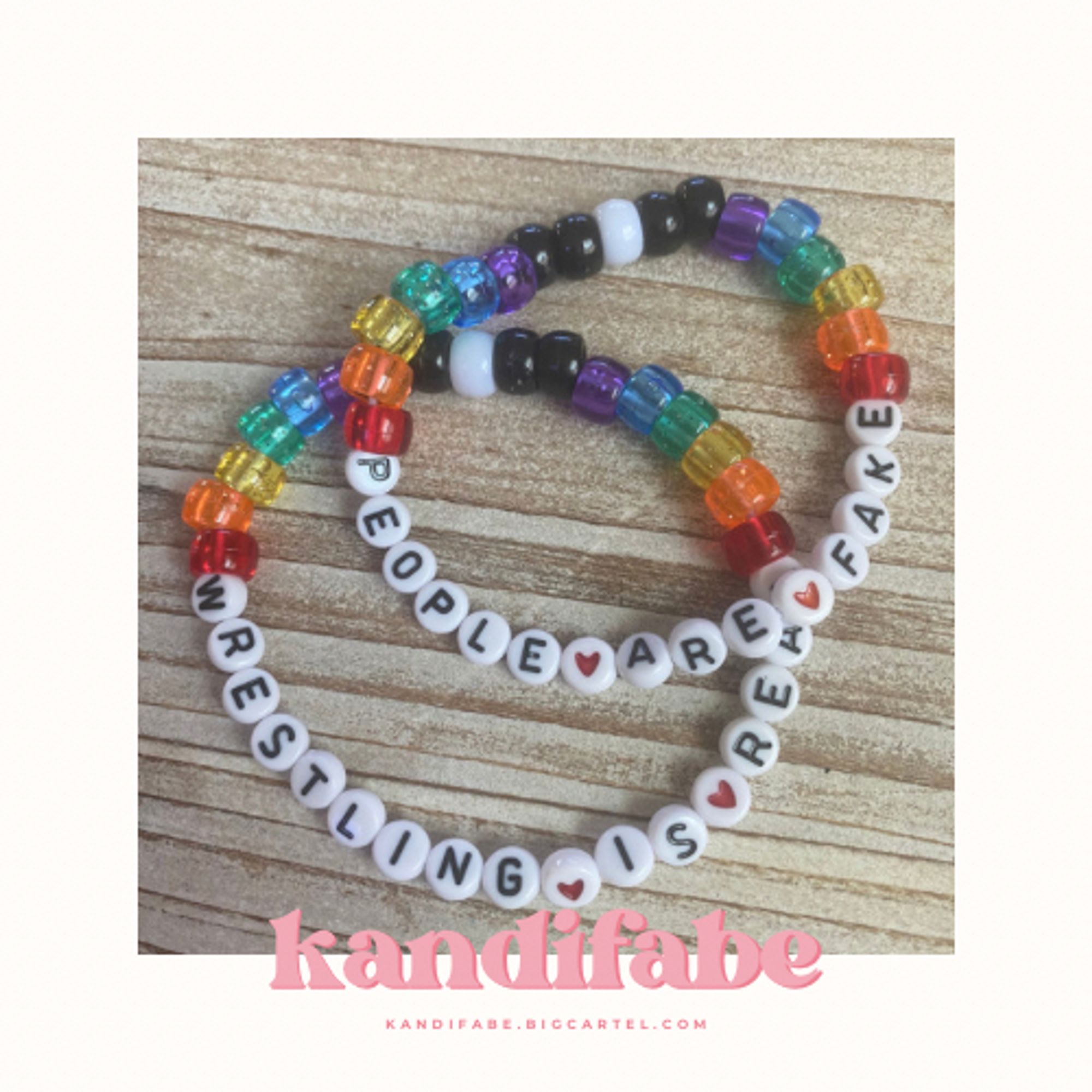 A pair of kandi bracelets that read “PEOPLE (red heart) ARE (red heart) FAKE” and “WRESTLING (red heart) IS (red heart) REAL” in black letters on white circle beads. The bracelets are filled in with translucent ROYGBV and opaque black and white pony beads.