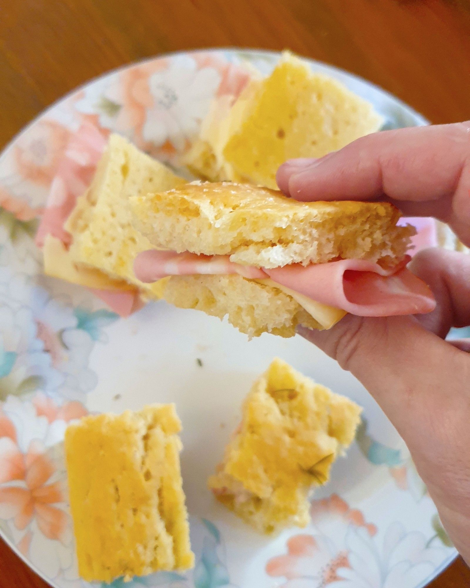 Holding a small slice of homemade focaccia stuffed with mortadella and scamorza cheese over a plate with other slices