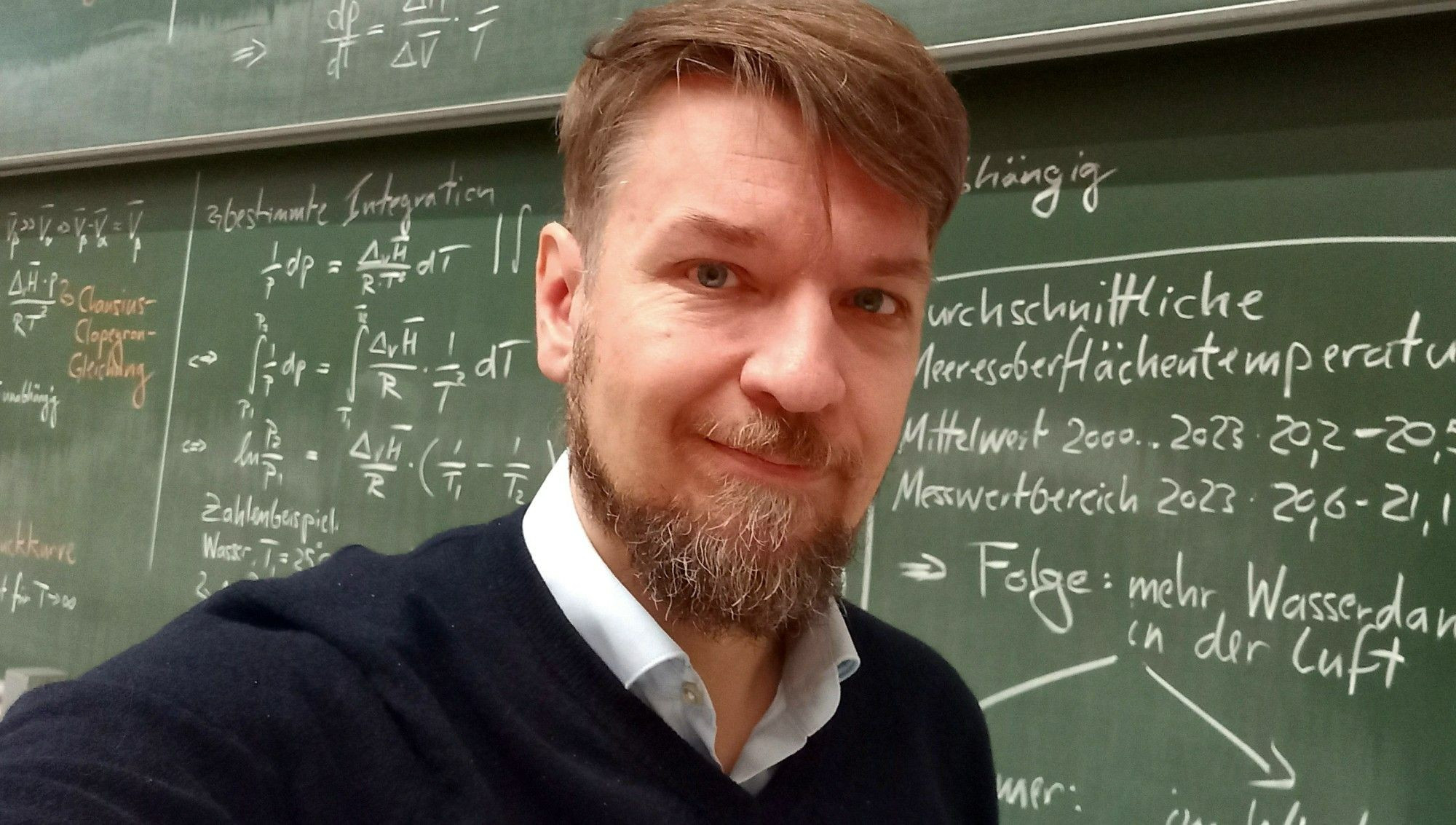 Selfie vor vollgeschriebener Kreidetafel im Chemie-Hörsaal der Uni Mainz nach meiner Grundvorlesung Physikalische Chemie zum Thema Clausius-Clapeyron-Gleichung im Wintersemester 2023/24. Auf der Tafel ist die bestimmte Integration der Clapeyron-Gleichung mitsamt Rechenbeispiel dargestellt. Daraus geht hervor, dass bei einer Meerestemperaturerhöhung von 1°C der Wassergehalt der Luft um 6% steigt. Dies bewirkt stärkere Niederschläge — je nach Lufttemperatur in Form von starkem Regen oder Schnee.