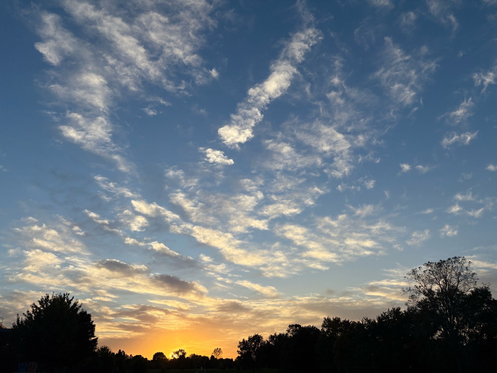 The sun sets in a lightly cloudy sky over London, Ontario, Canada.