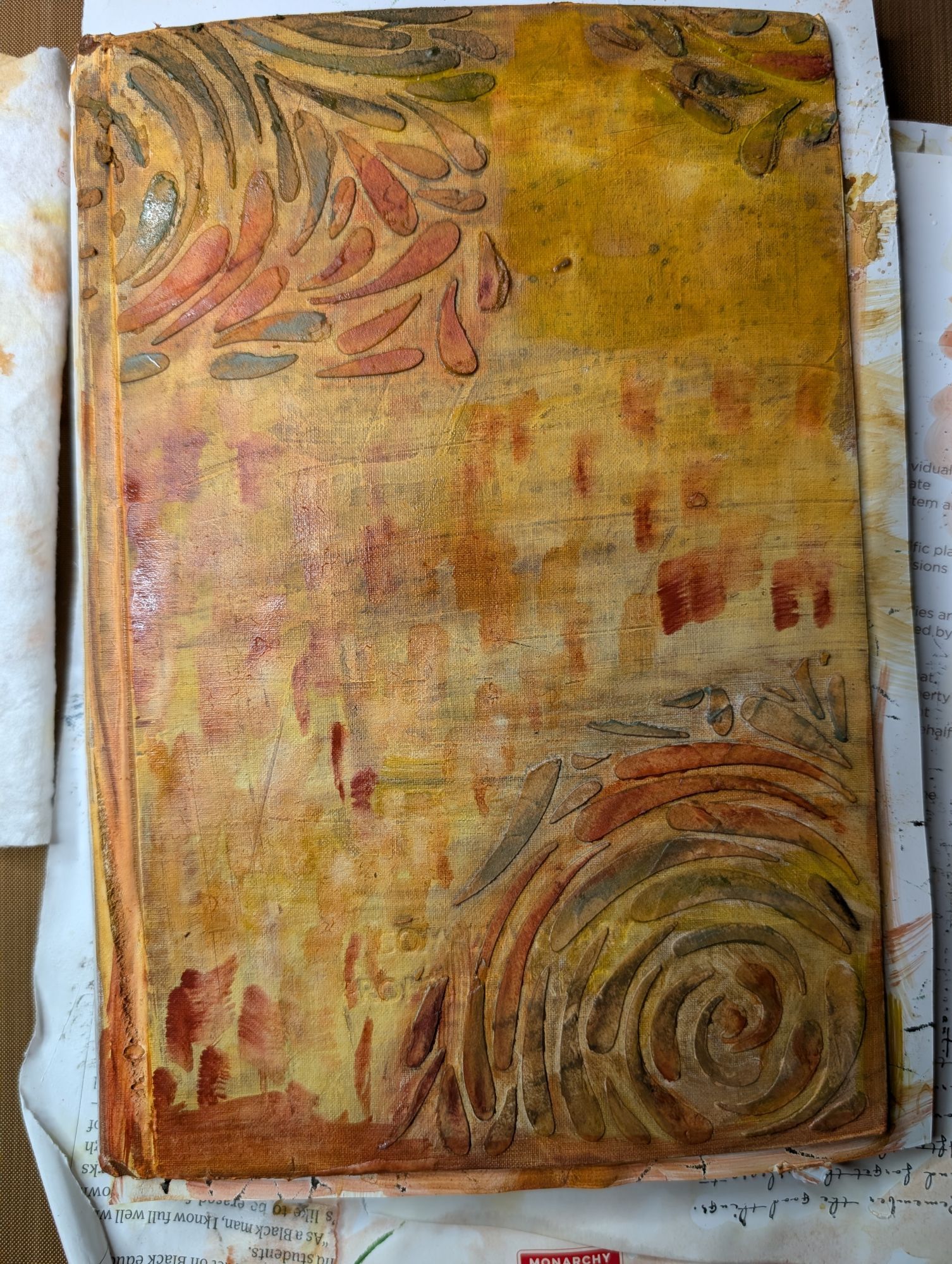 photo of cover as of today: it's been colored in various neutral brownish, yellowish & reddish/orange paint. I used Art Graf Water Soluble Tailors Chalk Shaped paint in earth tones. The floral stencil is highlighted in more saturated colors, using Tim Holtz Distress crayons in various brown & red shades.