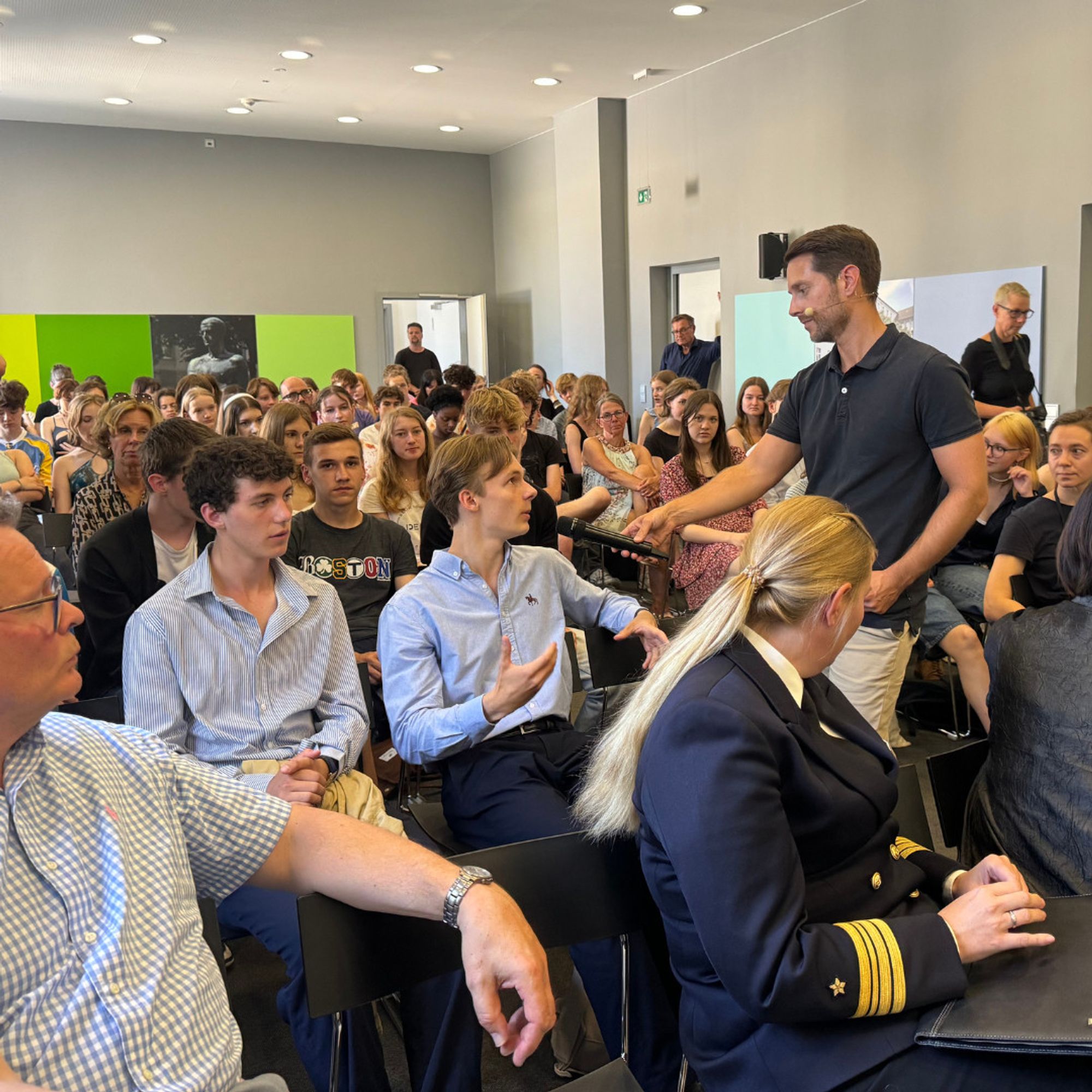 Blick in den bis auf den letzten Platz gefüllten Veranstaltungsraum der Gedenkstätte Deutscher Widerstand während der Diskussion mit Schülerinnen und Schülern nach der Filmvorführung. Mirko Drotschmann steht zwischen den Stuhlreihen und hält einem Schüler, der spricht und gestikuliert, ein Mikrofon entgegen. 
© Gedenkstätte Deutscher Widerstand