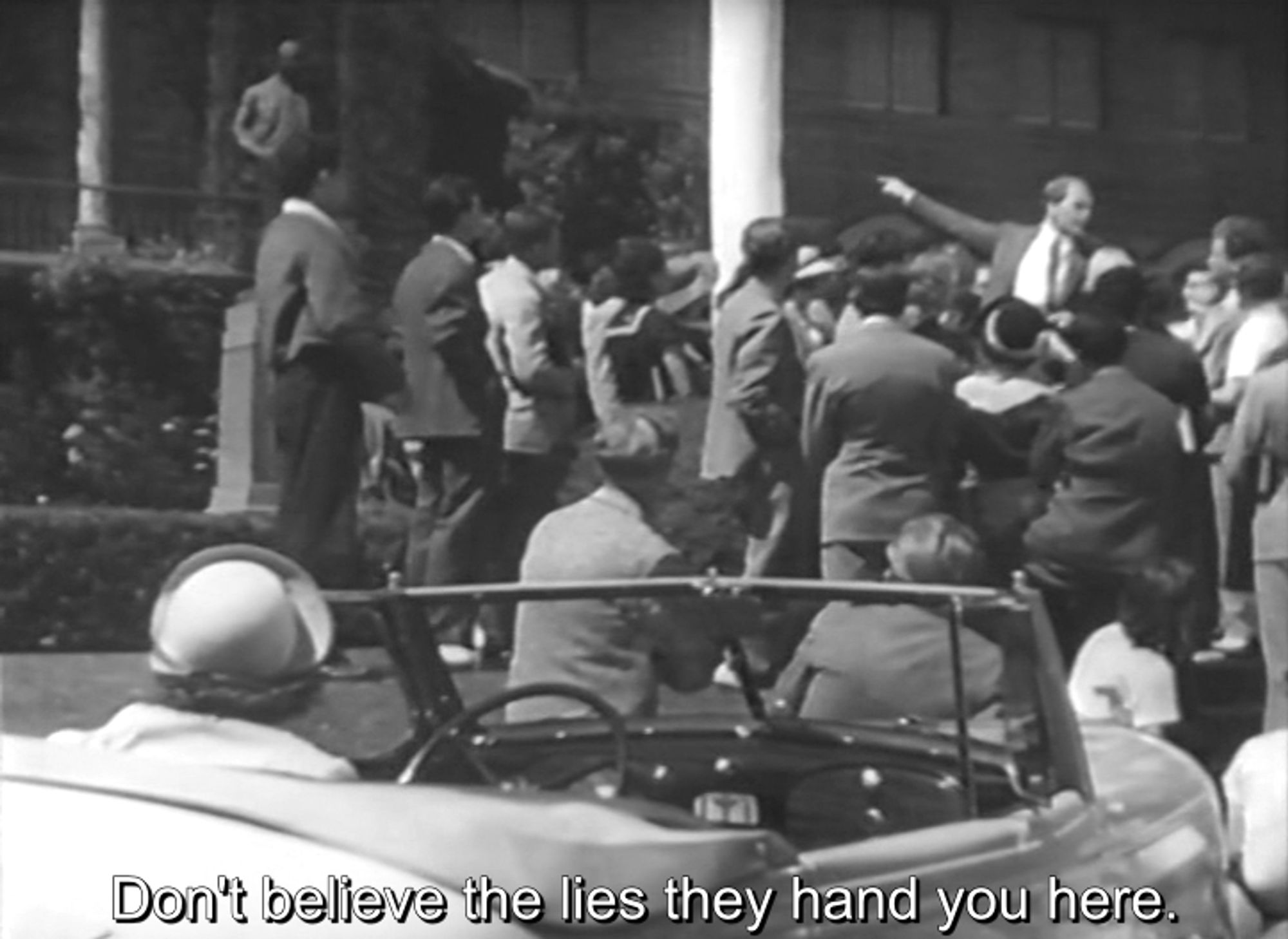 Red Salute (1935). Robert Young off in the distance gesturing dramatically, surrounded by a crowd of listeners. In the foreground, Barbara Stanwyck in her convertible, listening to his speech. He says, "Don't believe the lies they hand you here."