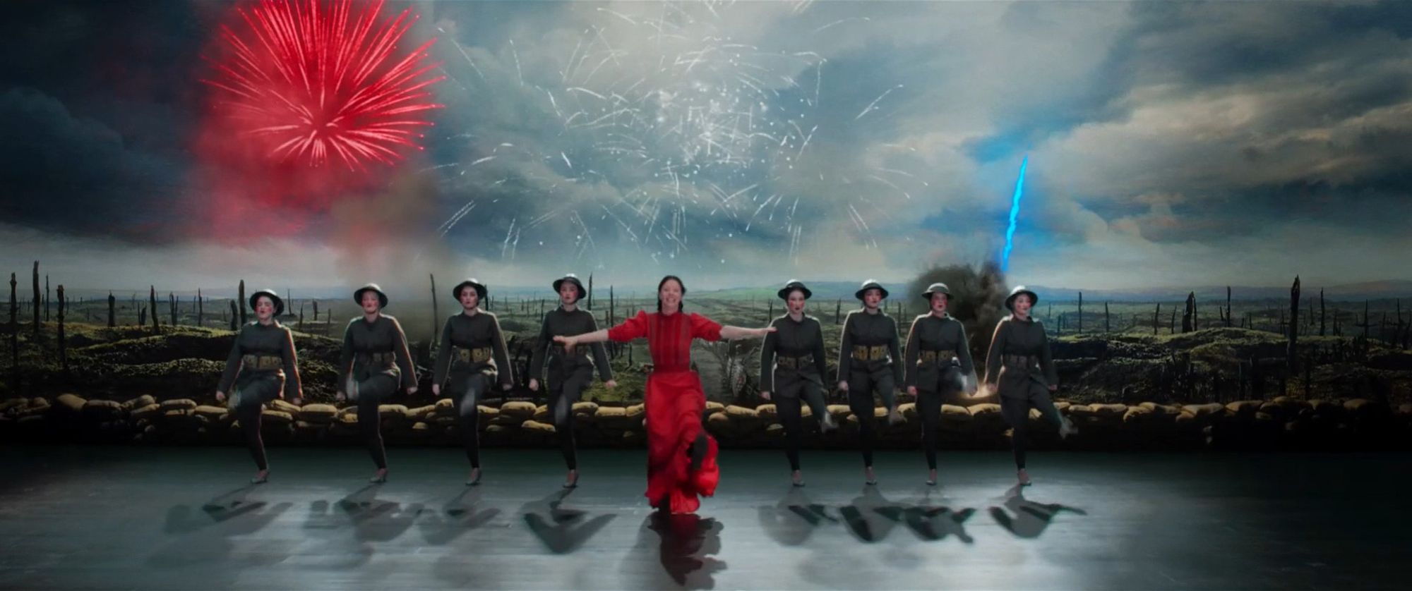 Pearl (2022). Pearl on stage in a red dress, imagining the war-torn battlefields of Europe behind her. She's in front of a kickline of women dressed to look like soldiers in the great war, but with whitened faces and doll-like red circles on their cheeks.