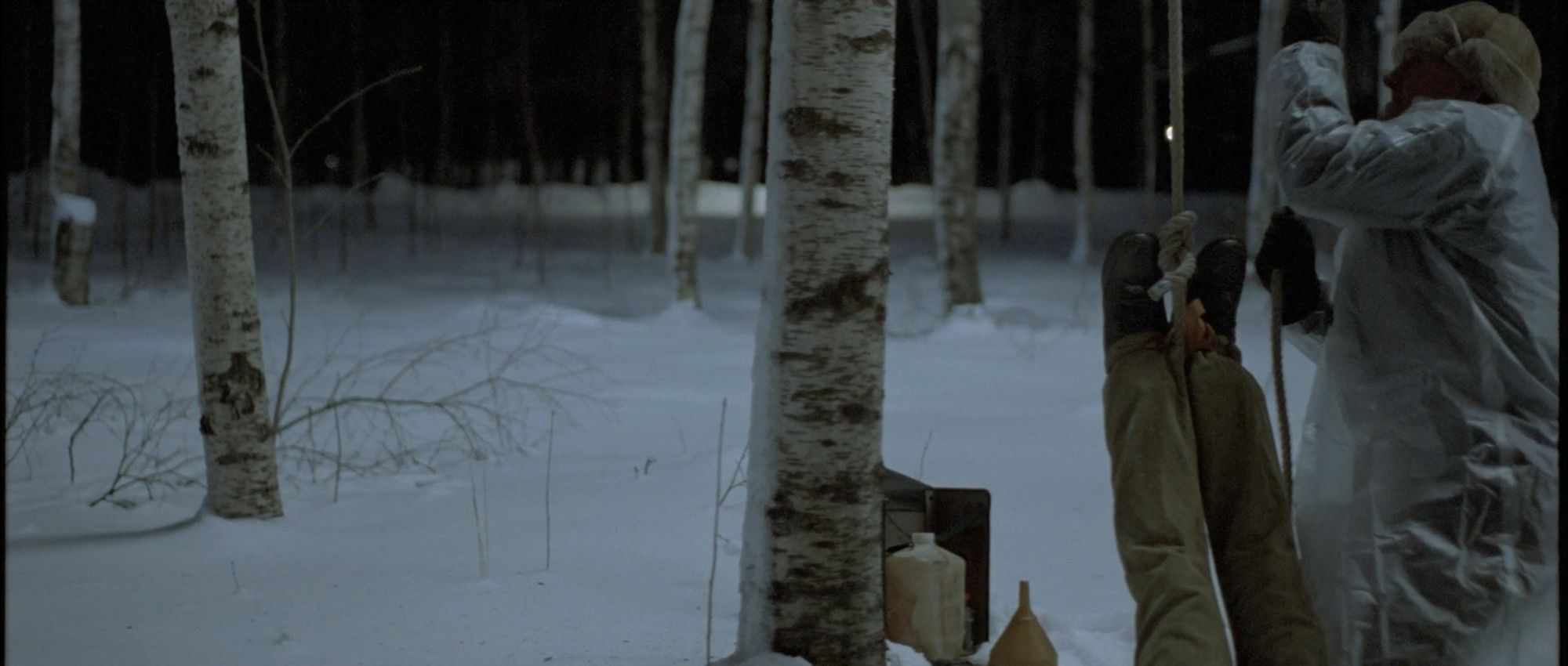 Let the Right One In (2008). In a snowy stand of birch trees, a man in a raincoat pulls a rope to hang another man from a tree by his feet. In the background, a jug and a funnel.