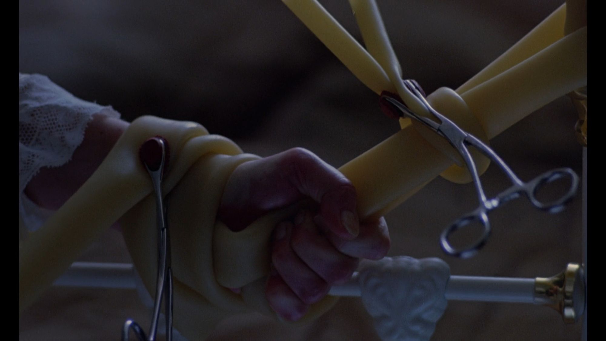 Dead Ringers (1988). A close-up of a hand bound to a cast iron bed frame with medical tubing and hemostats.