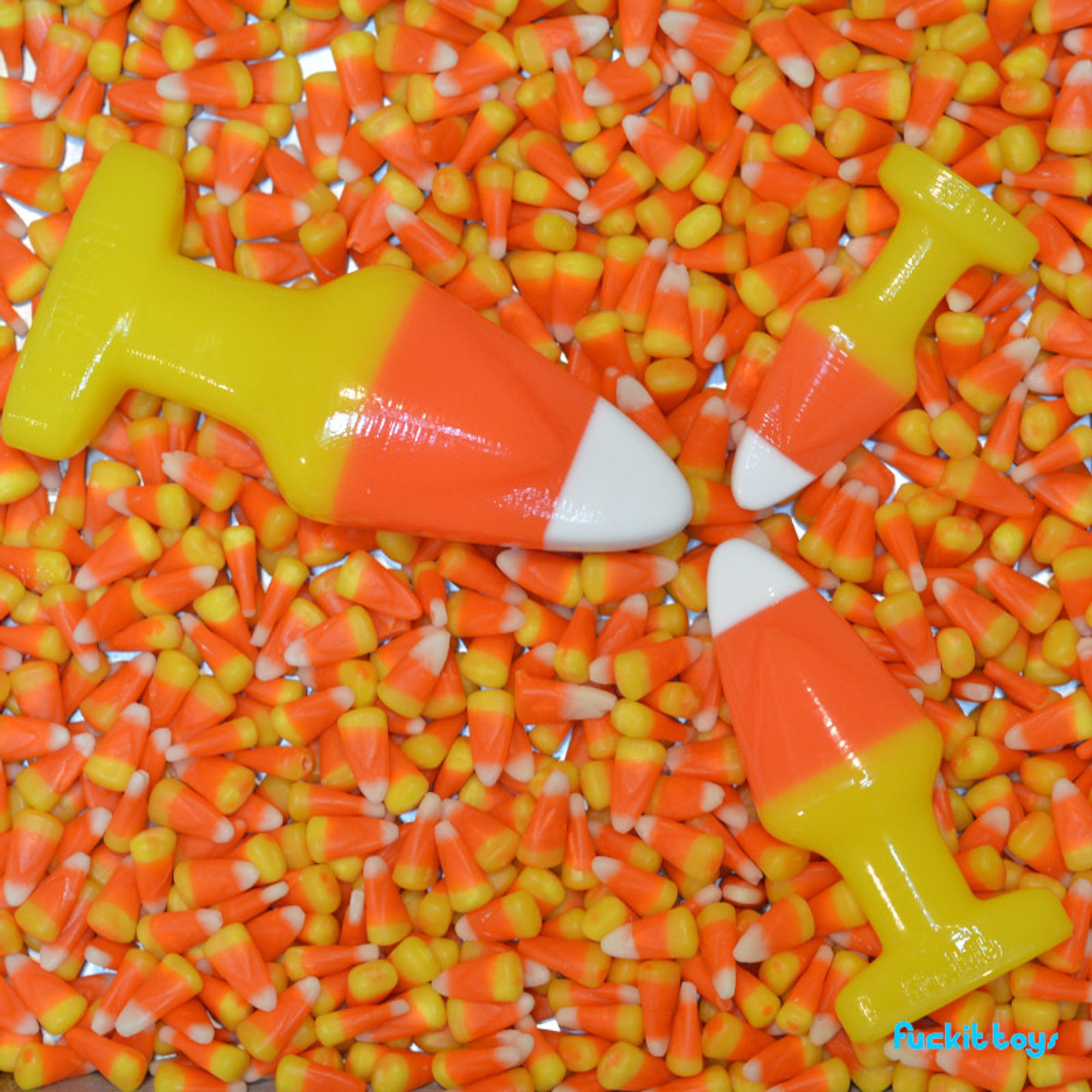 three candy corn buttplugs in different sizes, tip to tip on a field of actual candy corn.