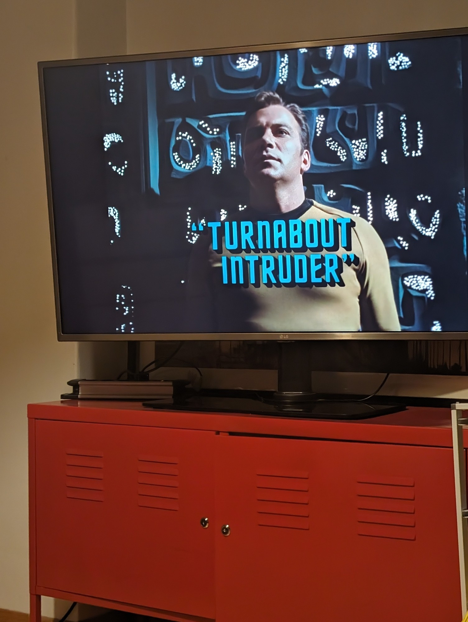 Photo of widescreen tv on top of red cupboard. The tv shows Star Trek scene with the character James T. Kirk and caption "Turnabout Intruder".