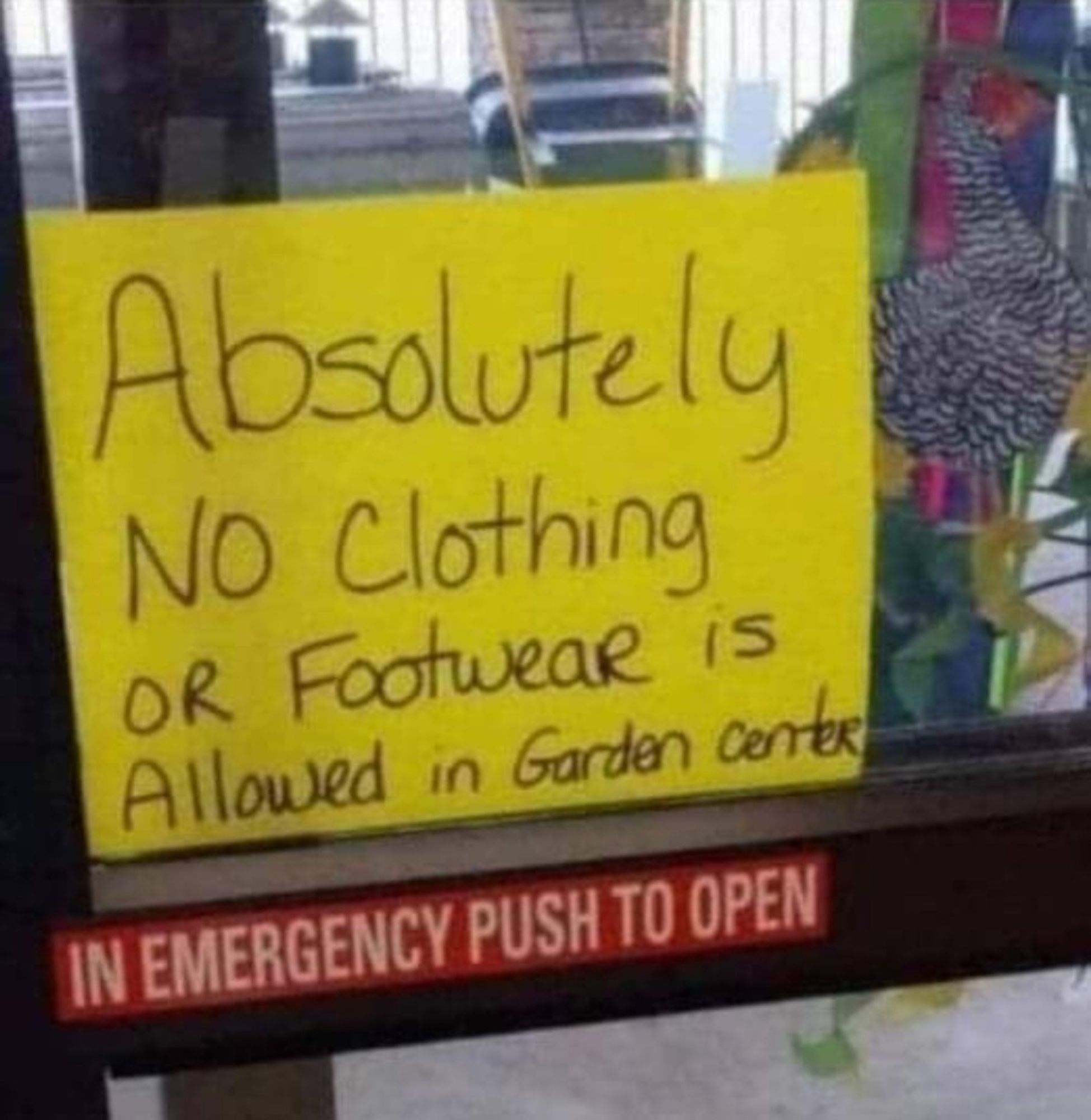 A yellow sign on a sliding glass door that reads: Absolutely No Clothing or Footwear is allowed in Garden Center.