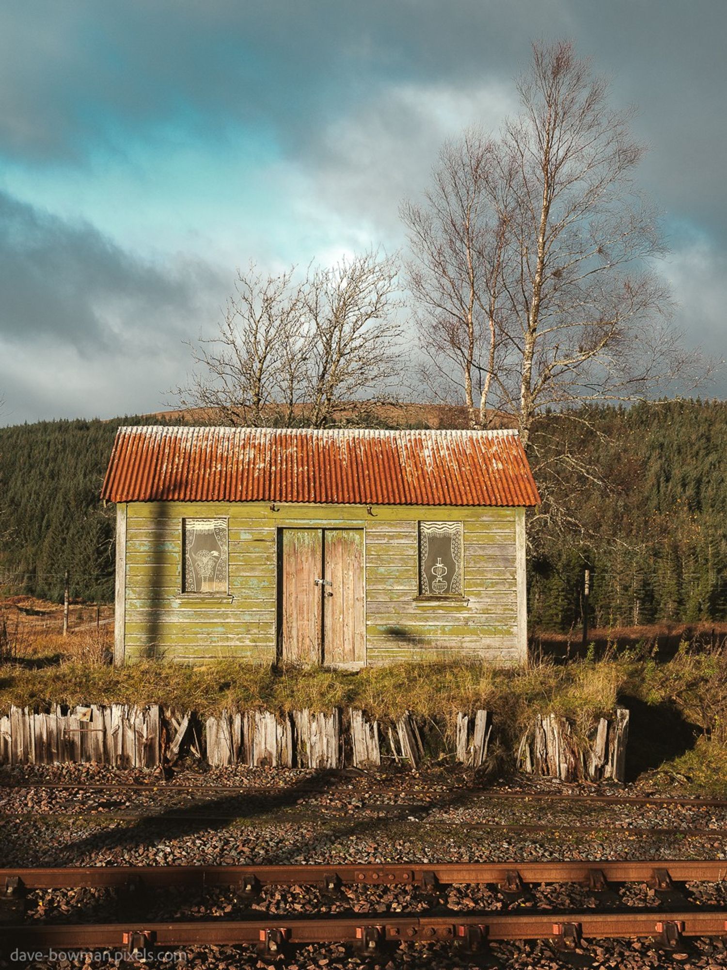 A colour photoghraph of he Platelayers Hut at Rannoch Station, a historic structure located in the remote Rannoch Moor area of Scotland. This small hut served as accommodation for railway workers, known as platelayers, who were responsible for maintaining and repairing the tracks in the early 20th century. Today, the Platelayers Hut stands as a testament to the bygone era of railway maintenance in a rugged and picturesque environment. It provides a glimpse into the laborious and often isolated life of those who worked on the railway lines, and is a unique point of interest for visitors exploring the stunning landscape of Scotland.