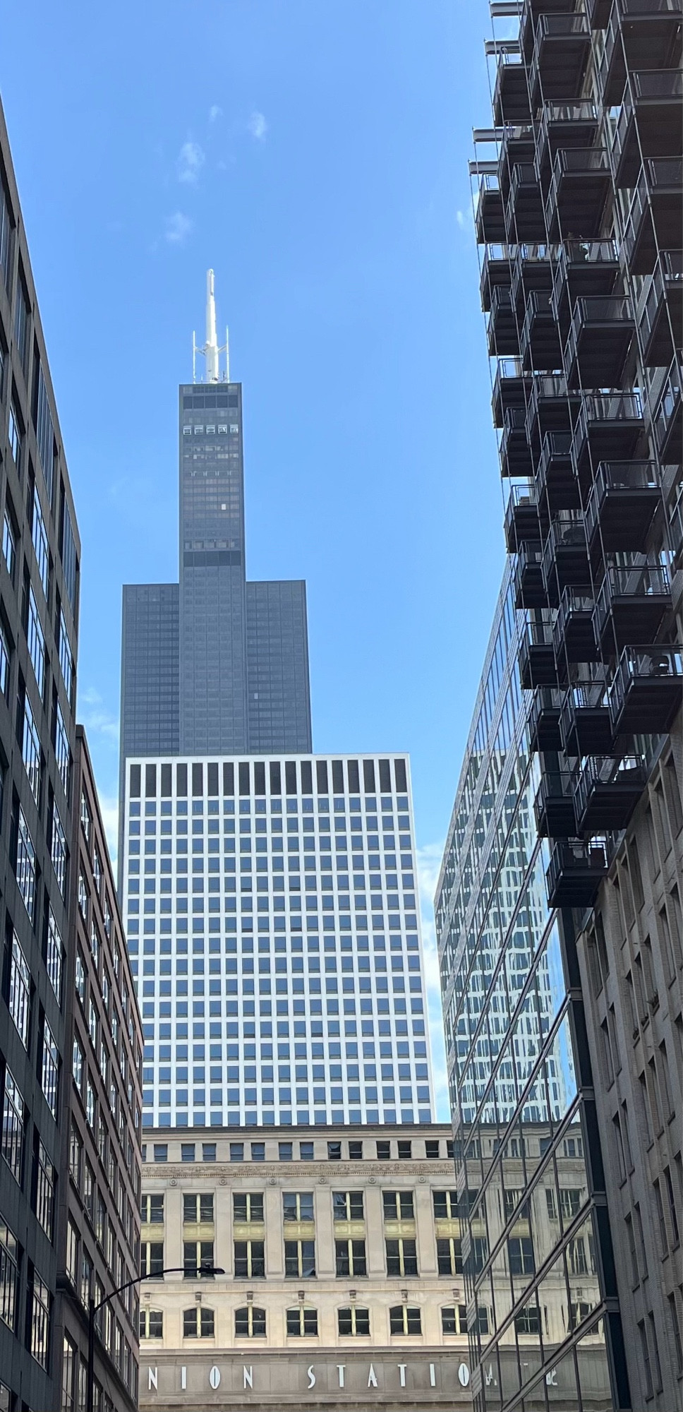 Sears tower shot from the west, with a blue sky and tiny clouds, framed by two buildings on either side, and Union Station in front