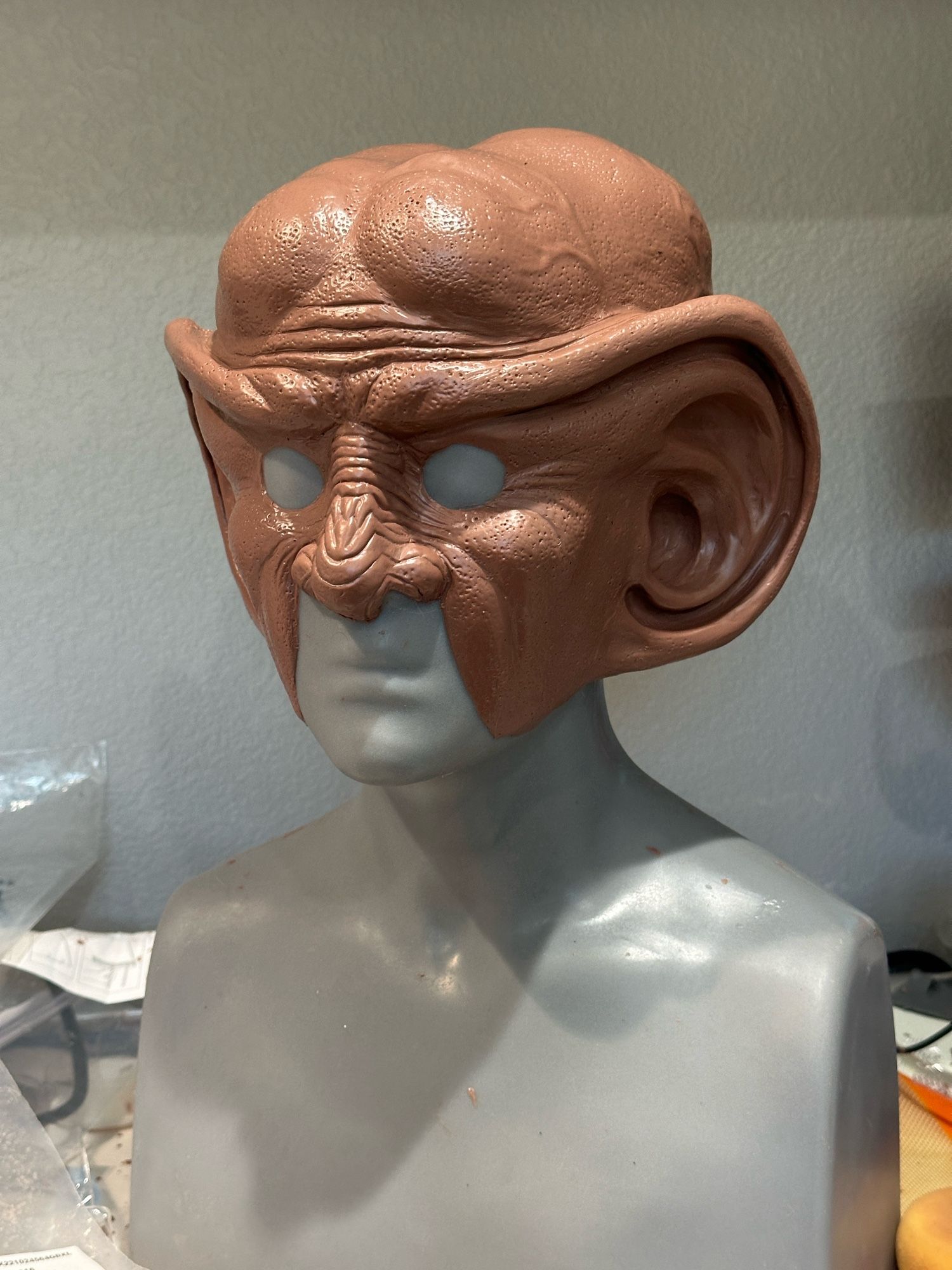 A 3/4 view of an in-progress Ferengi head sculpture. The clay is brown, and the human head it is sculpted onto is gray.