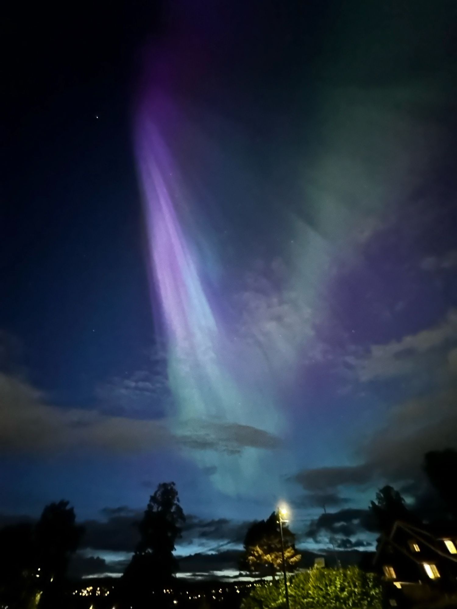 Aurora borealis and clouds over silhouettes of houses and trees