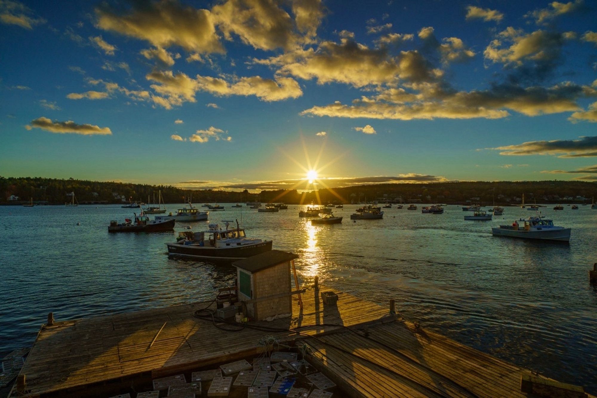 Lobster boats anchored in a harbor, sun in the middle of the shot with sunstars