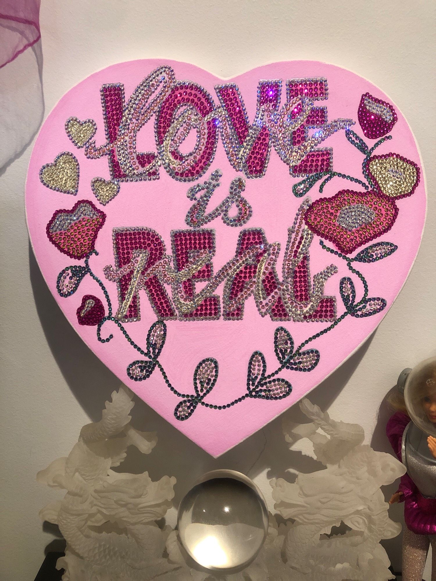 Light pink heart-shaped canvas with diamantés that say LOVE IS REAL, flowers and hearts, based on Chuck Tingle’s jacket design