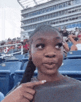 black girl at a ball game during the day time smiling and biting her nail 